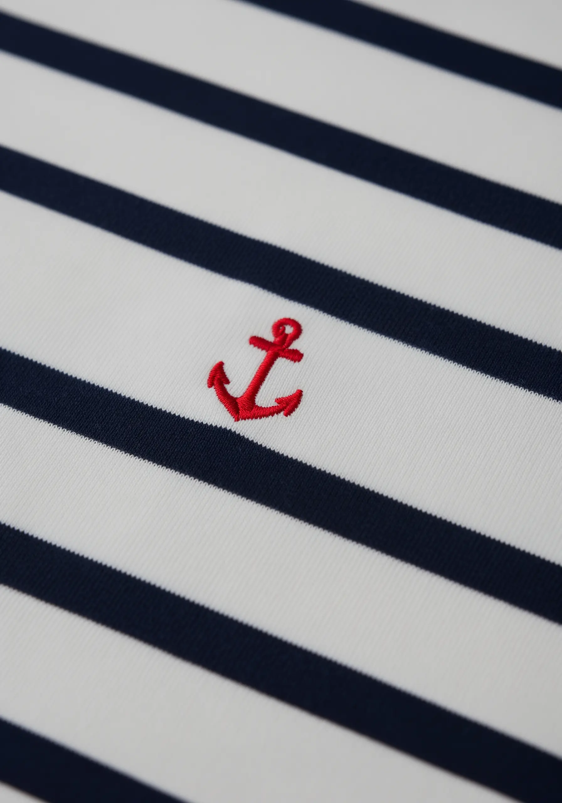 A small, bright red anchor embroidered on a navy and white striped polo shirt.