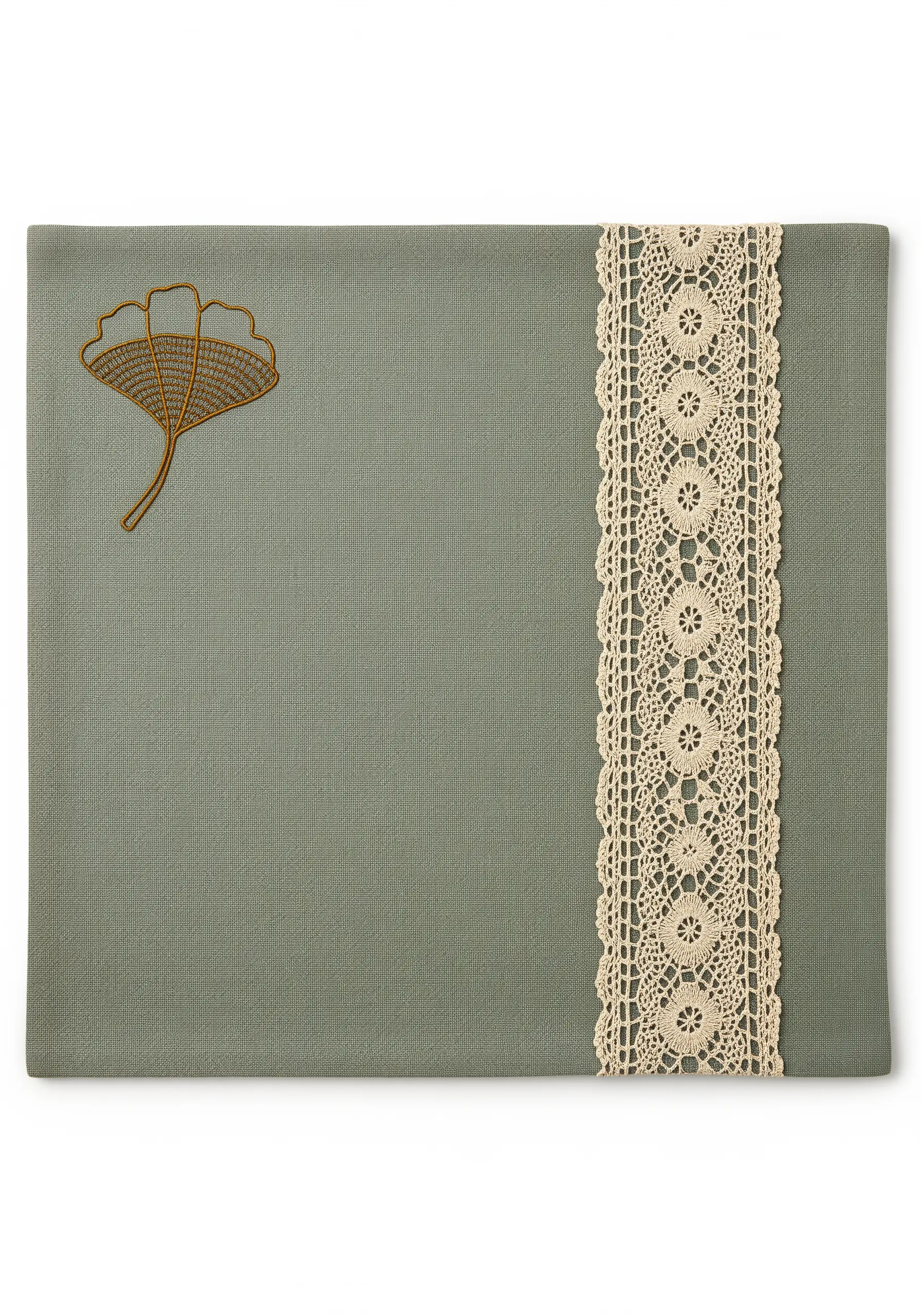 A single embroidered ginkgo leaf on a sage green placemat with a vertical lace strip.