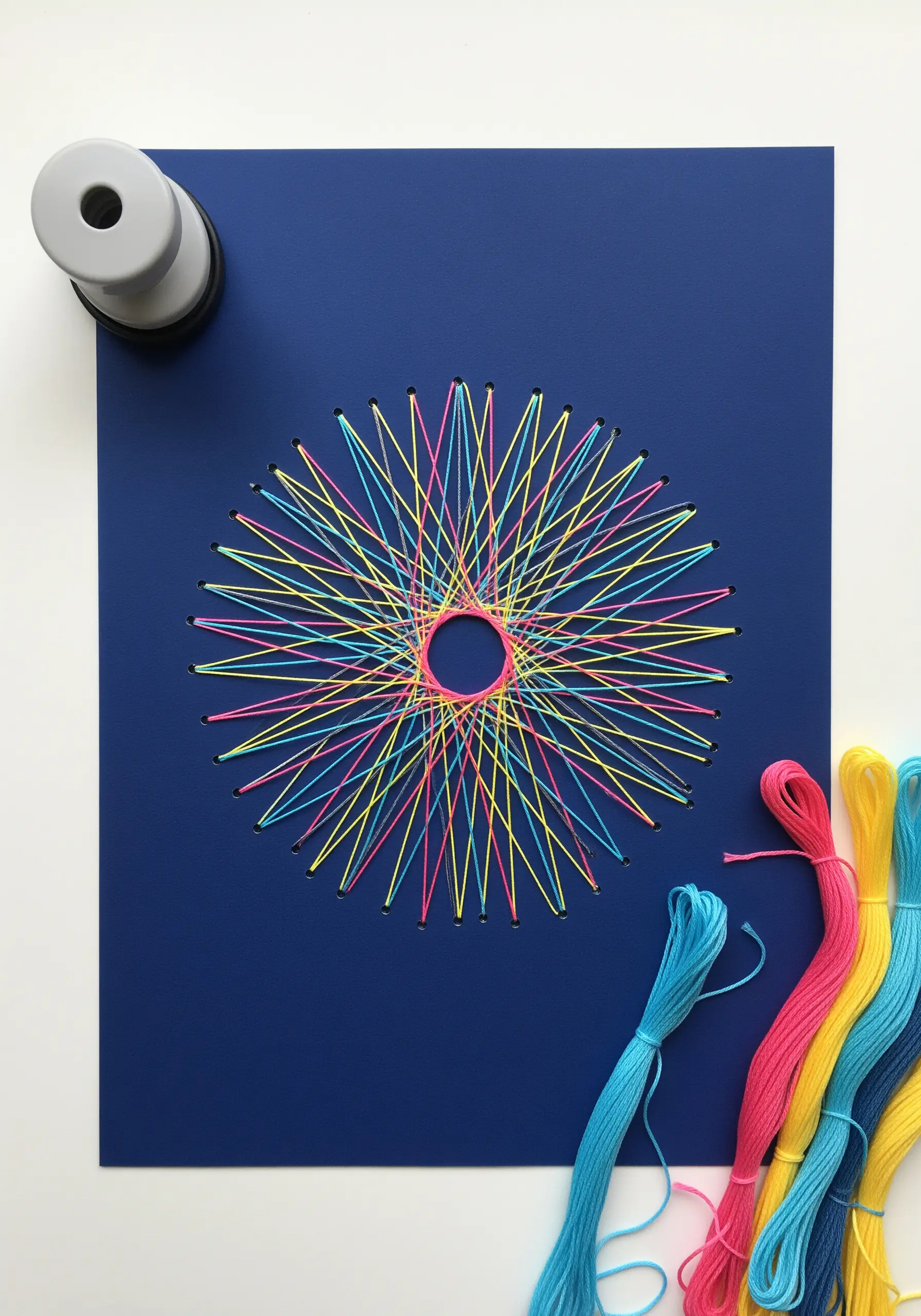 A vibrant geometric mandala made with string art techniques on a dark blue piece of paper.