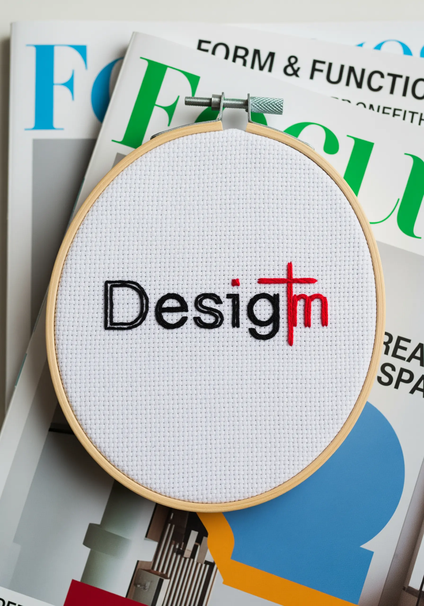 The word 'Design' embroidered with the 't' highlighted in red as a cross.
