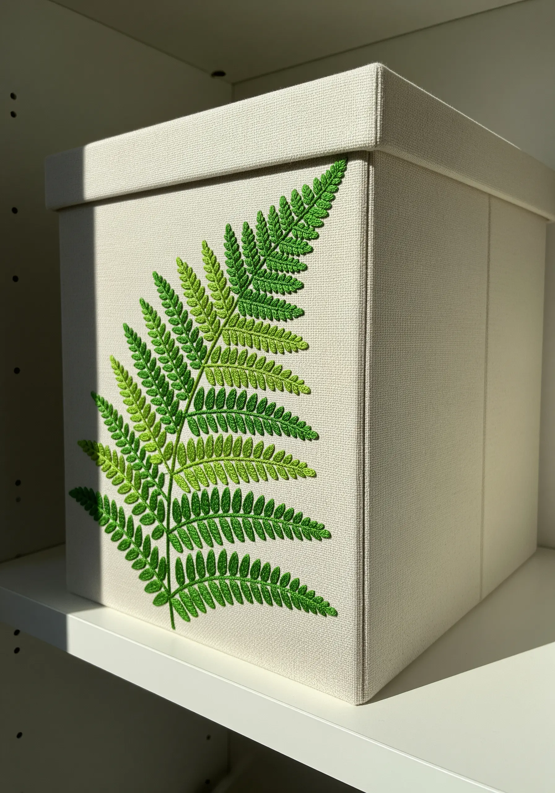 A realistic fern embroidered on a fabric box, using a gradient of green threads.