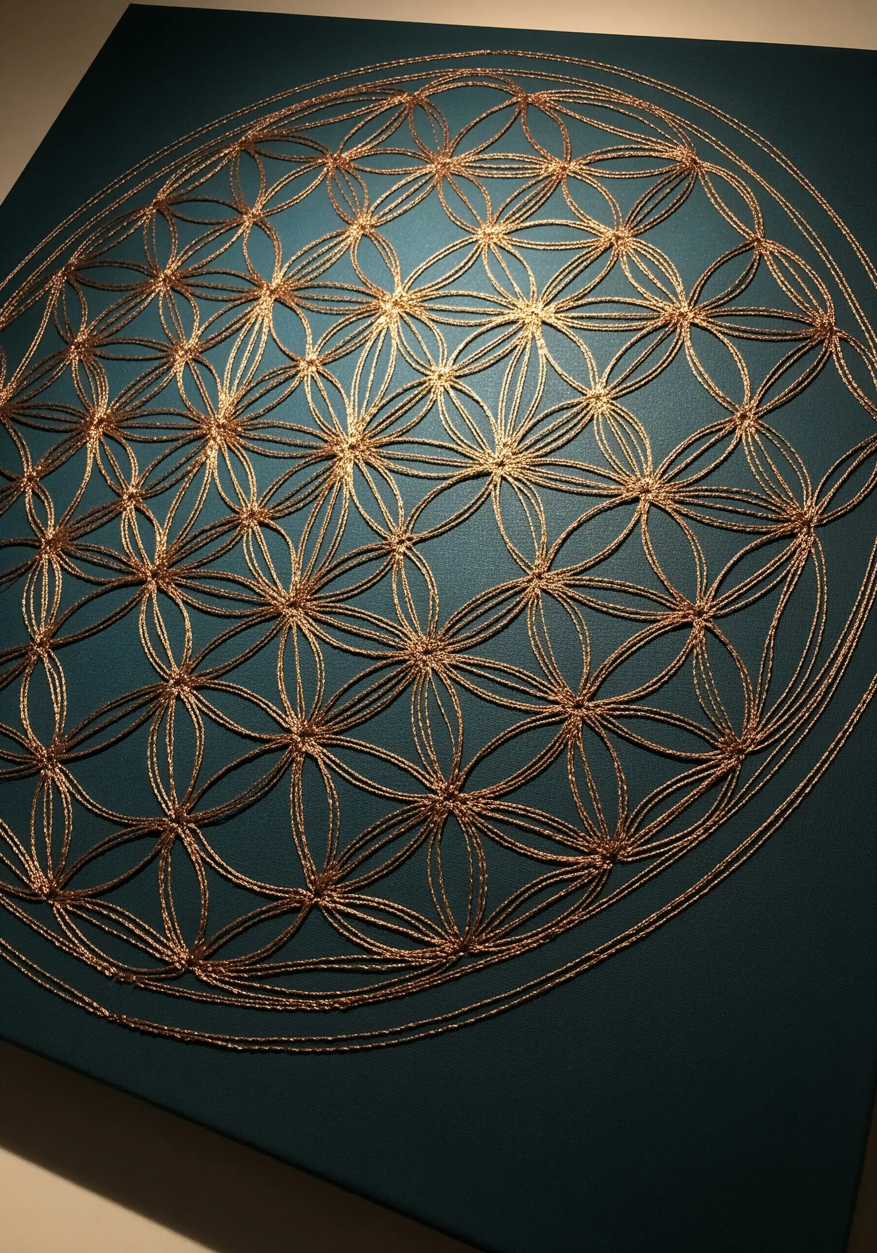 A golden Flower of Life pattern stitched in couched metallic cord on a teal canvas.