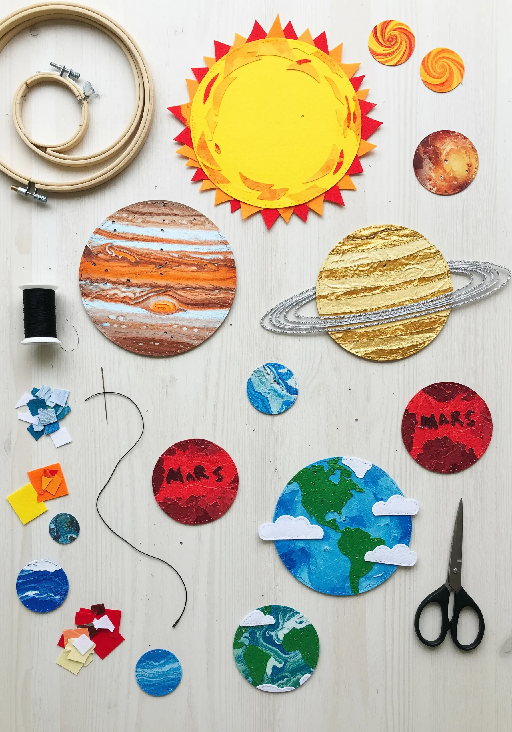 A solar system collage made from painted and textured paper, with thread and other craft supplies.