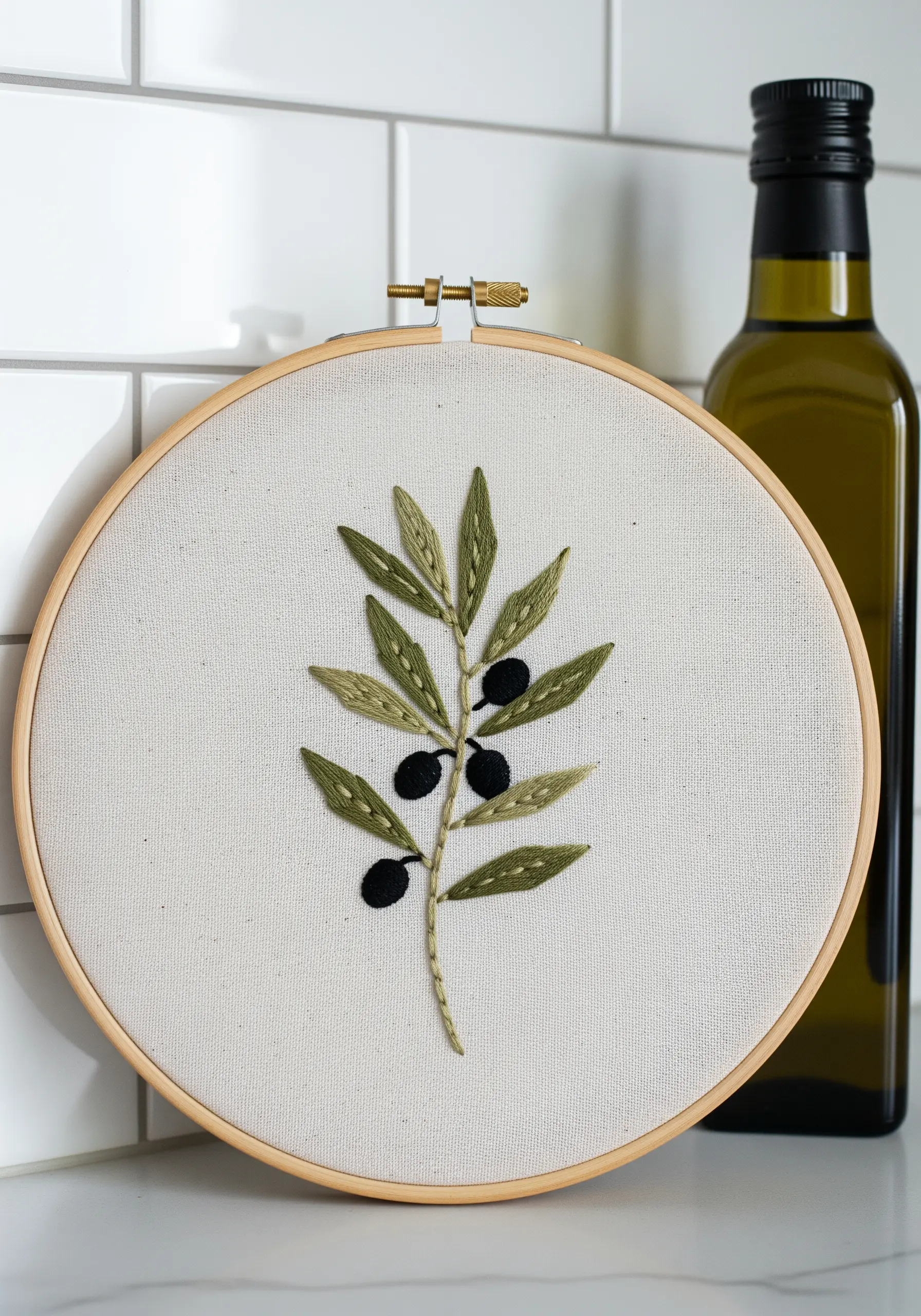 Embroidery of an olive branch with green fishbone stitch leaves and black satin stitch olives.