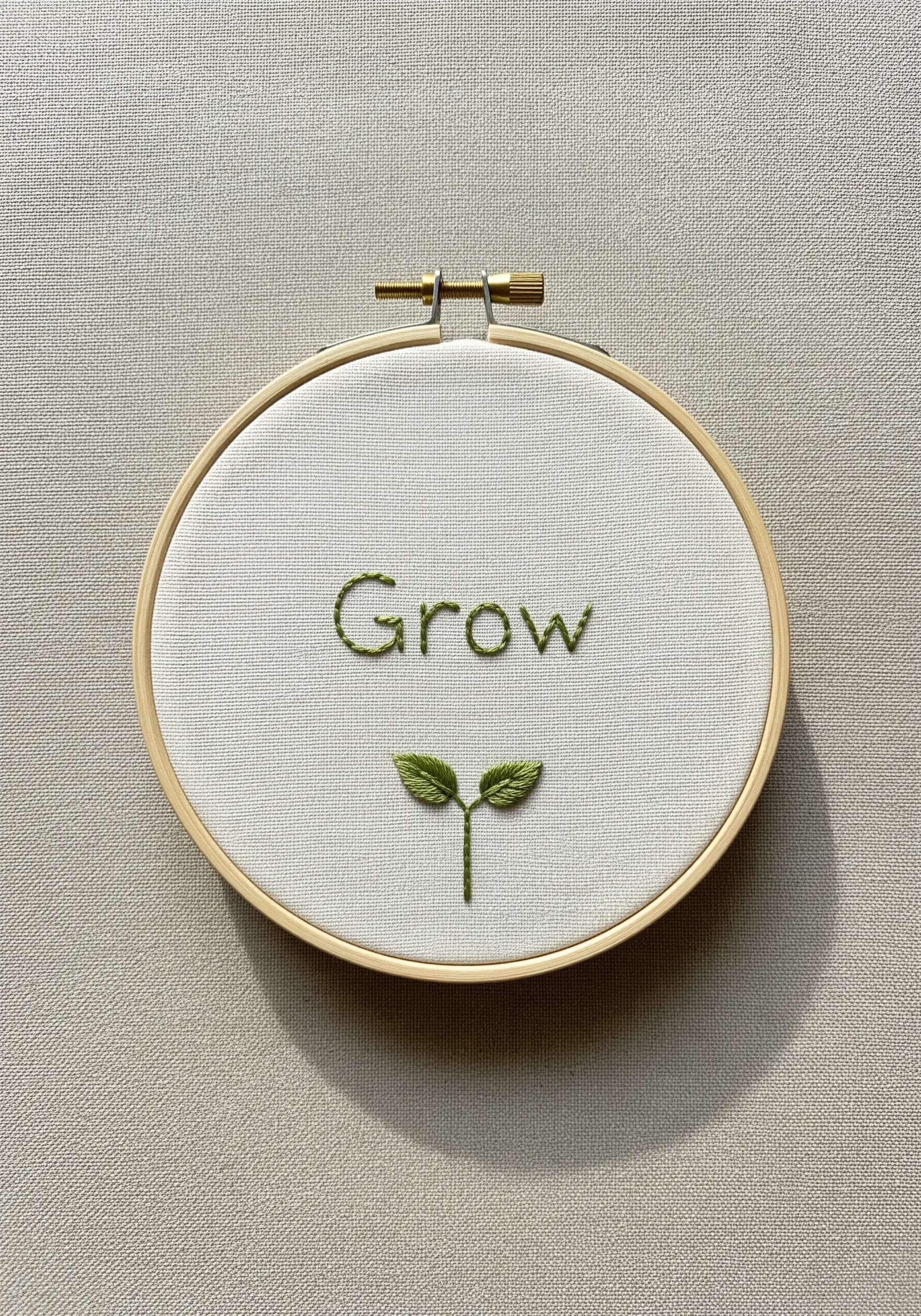 'Grow' embroidered in green with a small seedling stitched with fishbone stitch leaves.