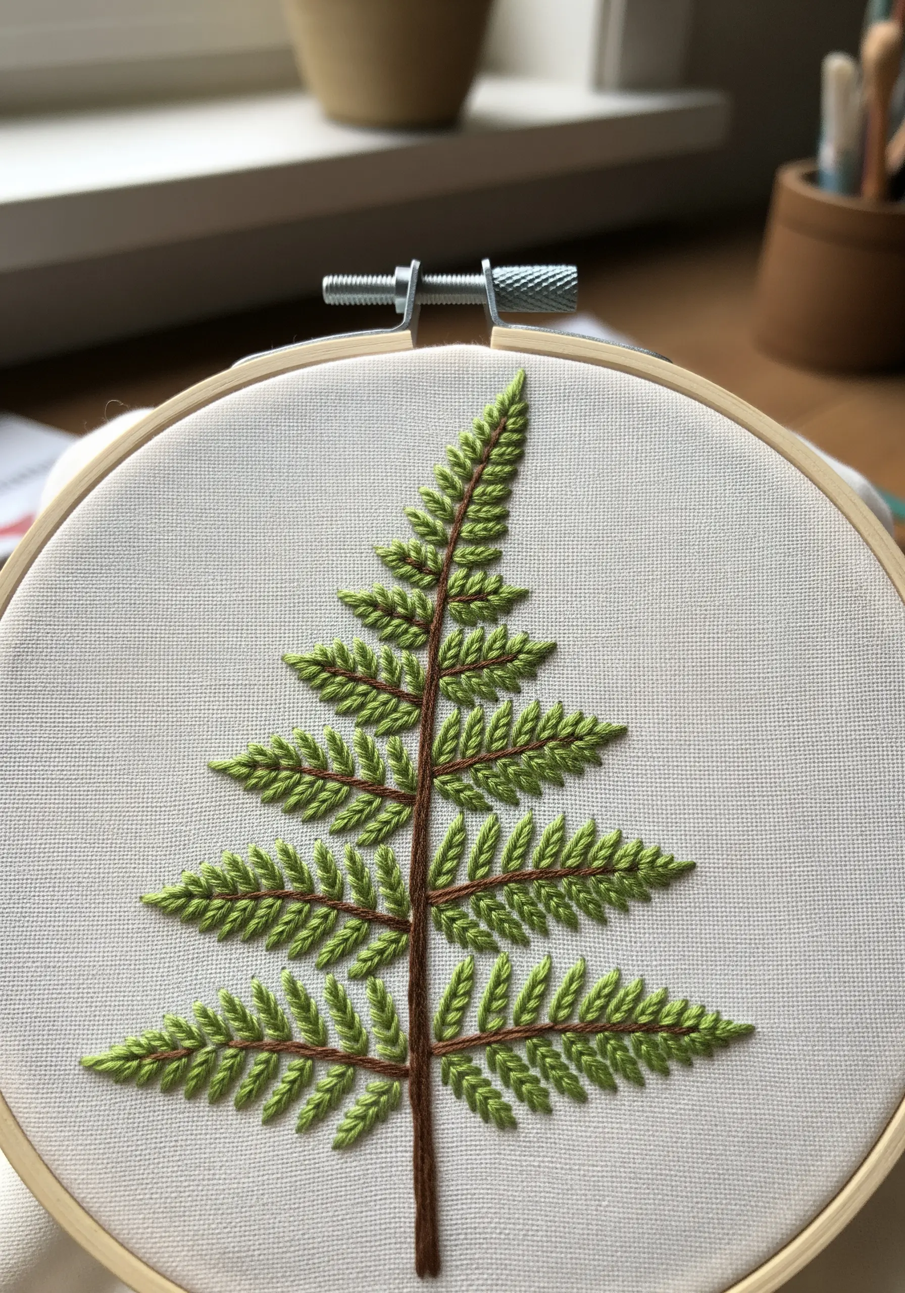 Fern leaf embroidered with green fishbone stitch and a brown stem.