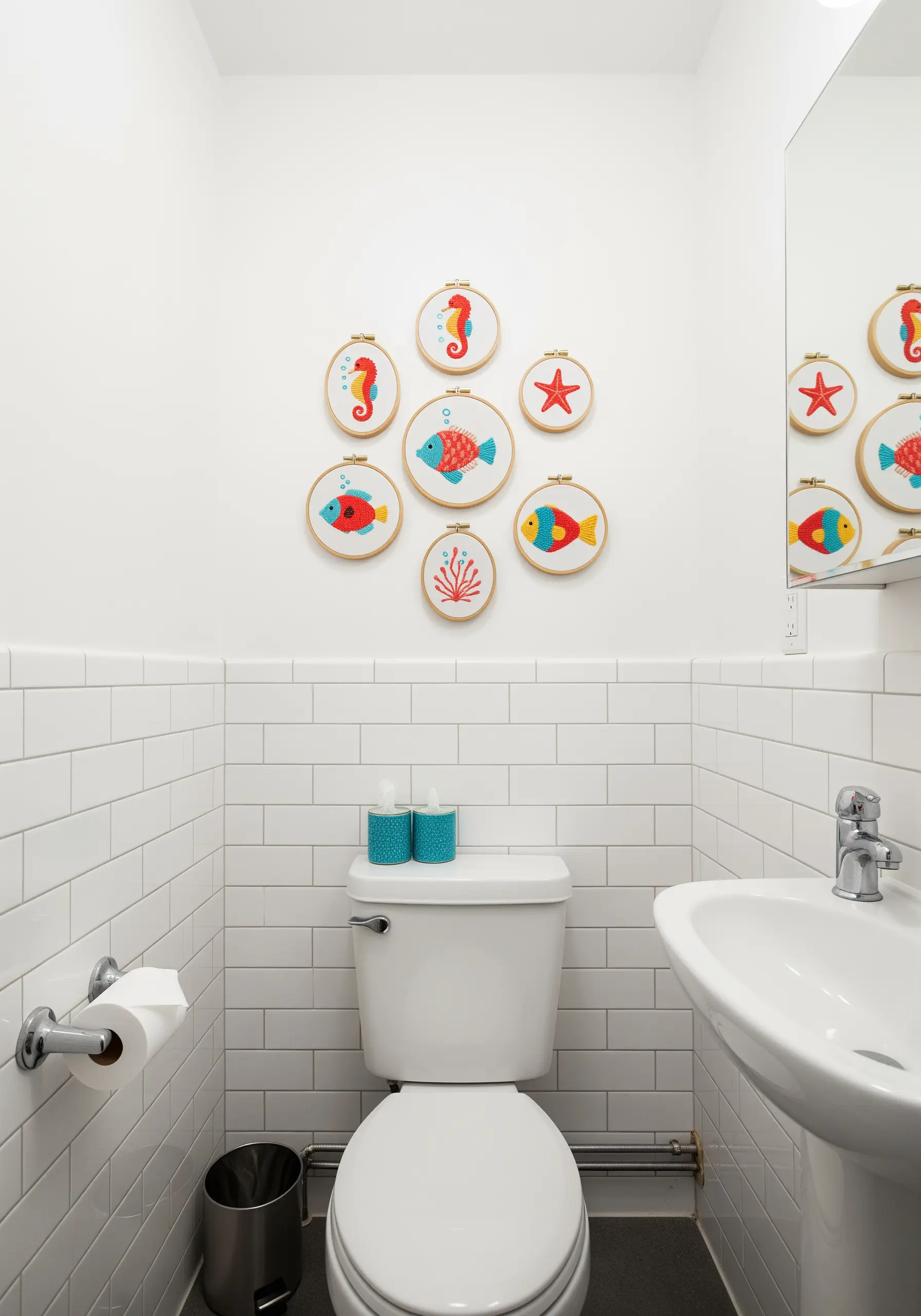 A collection of aquatic-themed embroidery hoops, including fish and a seahorse, on a white tile wall
