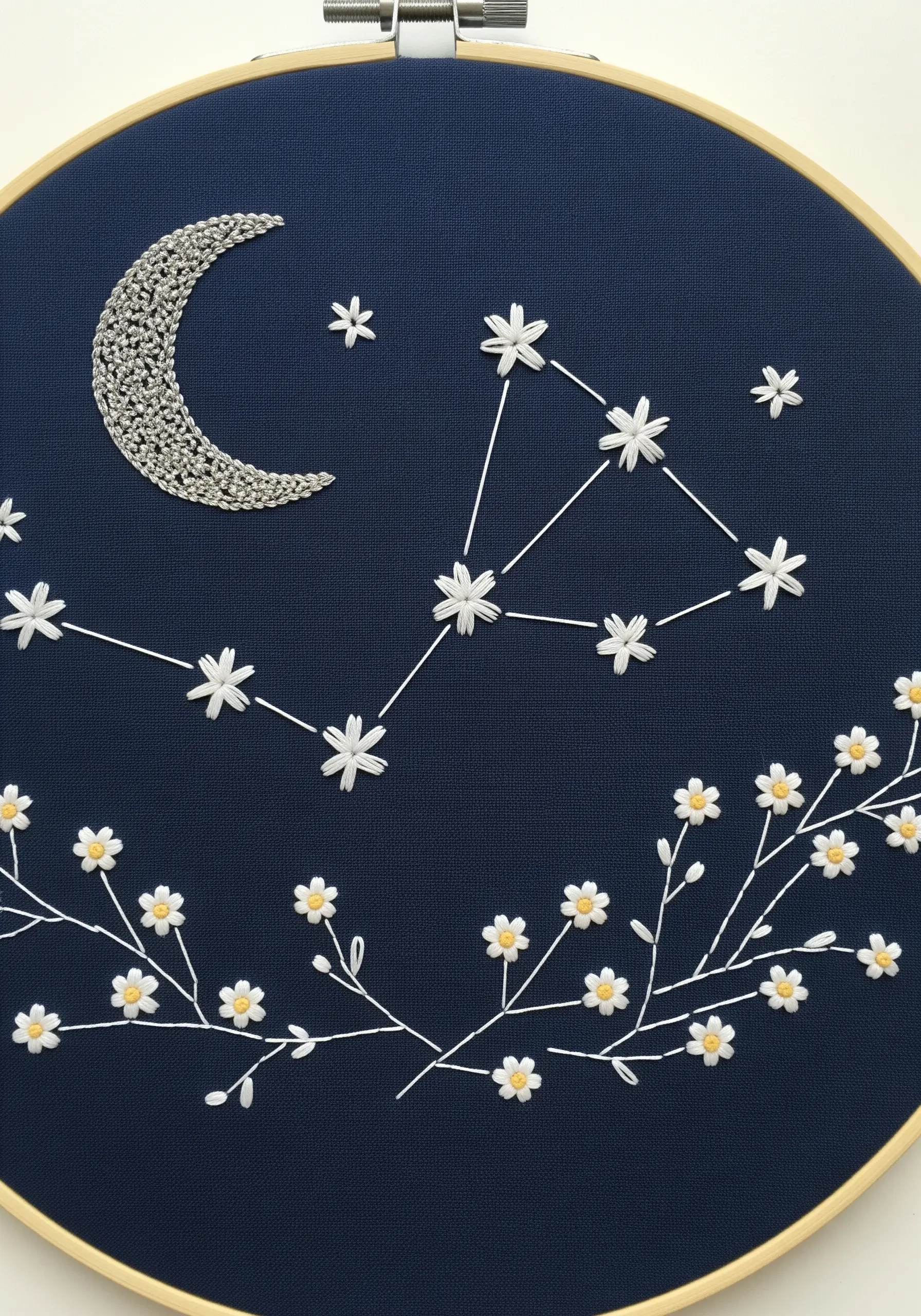 Embroidered moon and floral constellation with metallic thread on dark blue fabric.