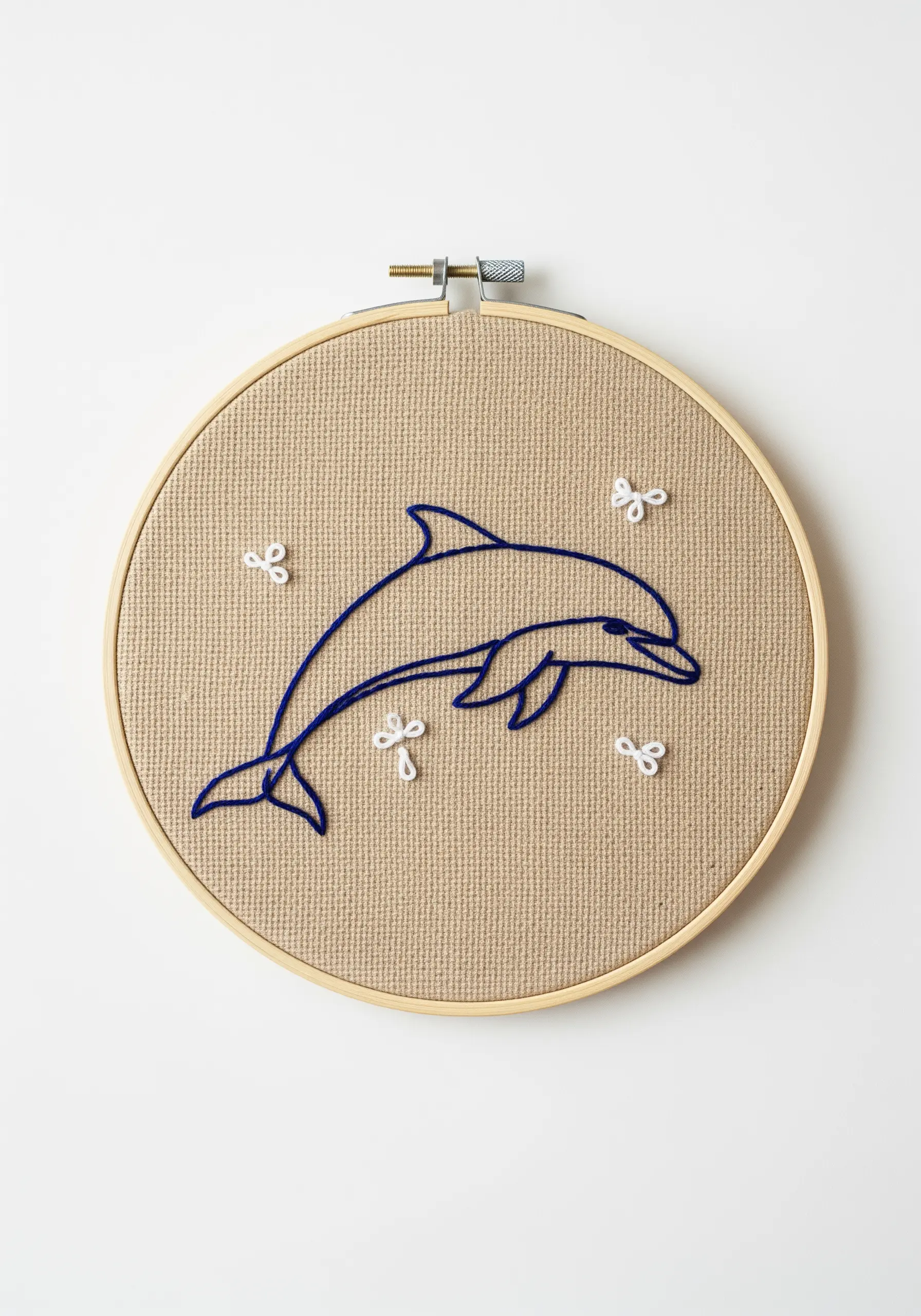 Minimalist dolphin outline in blue thread on brown linen, accented with small white stitches.