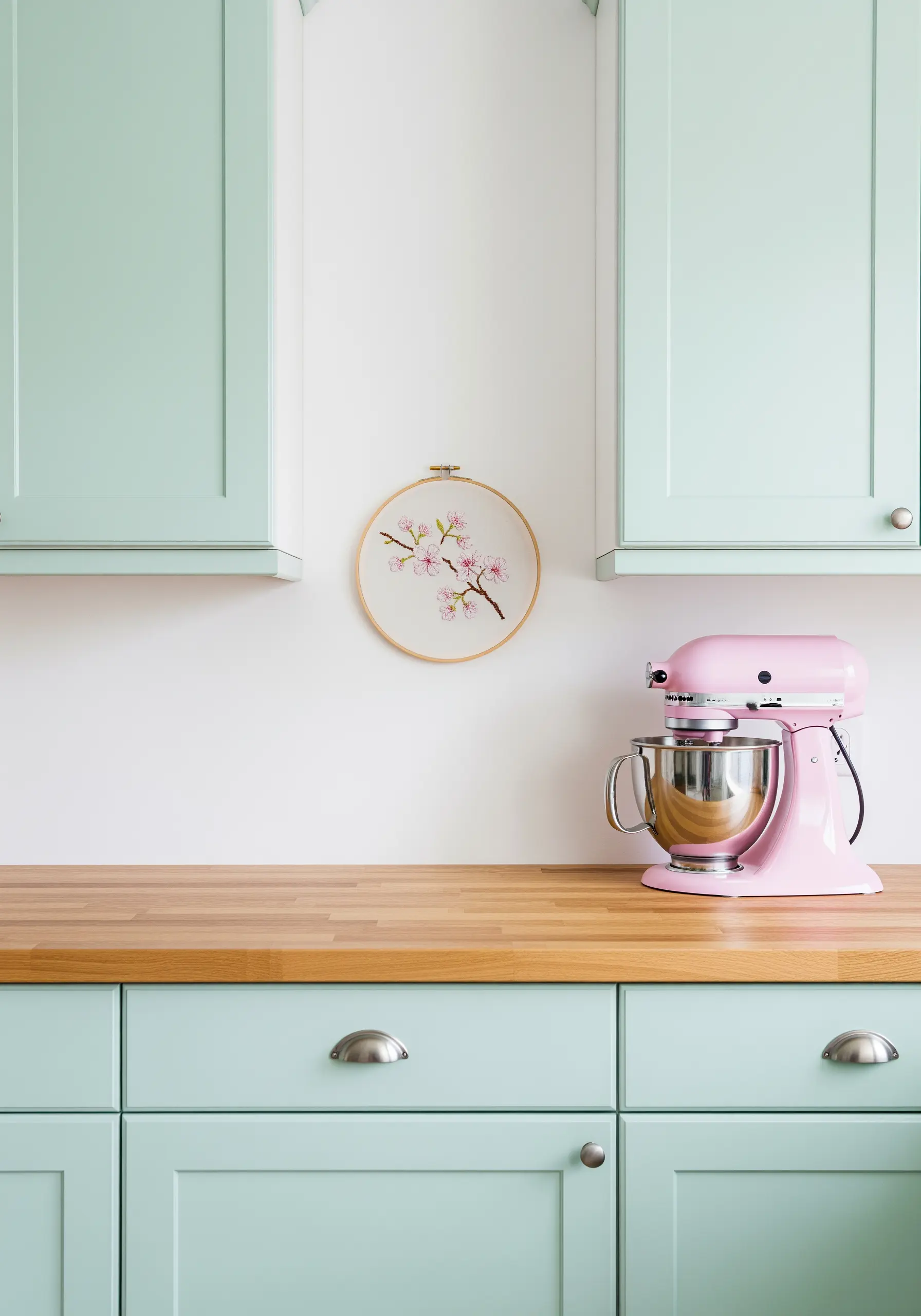 Minimalist embroidery of a cherry blossom branch in a hoop, in a mint green and pink kitchen.