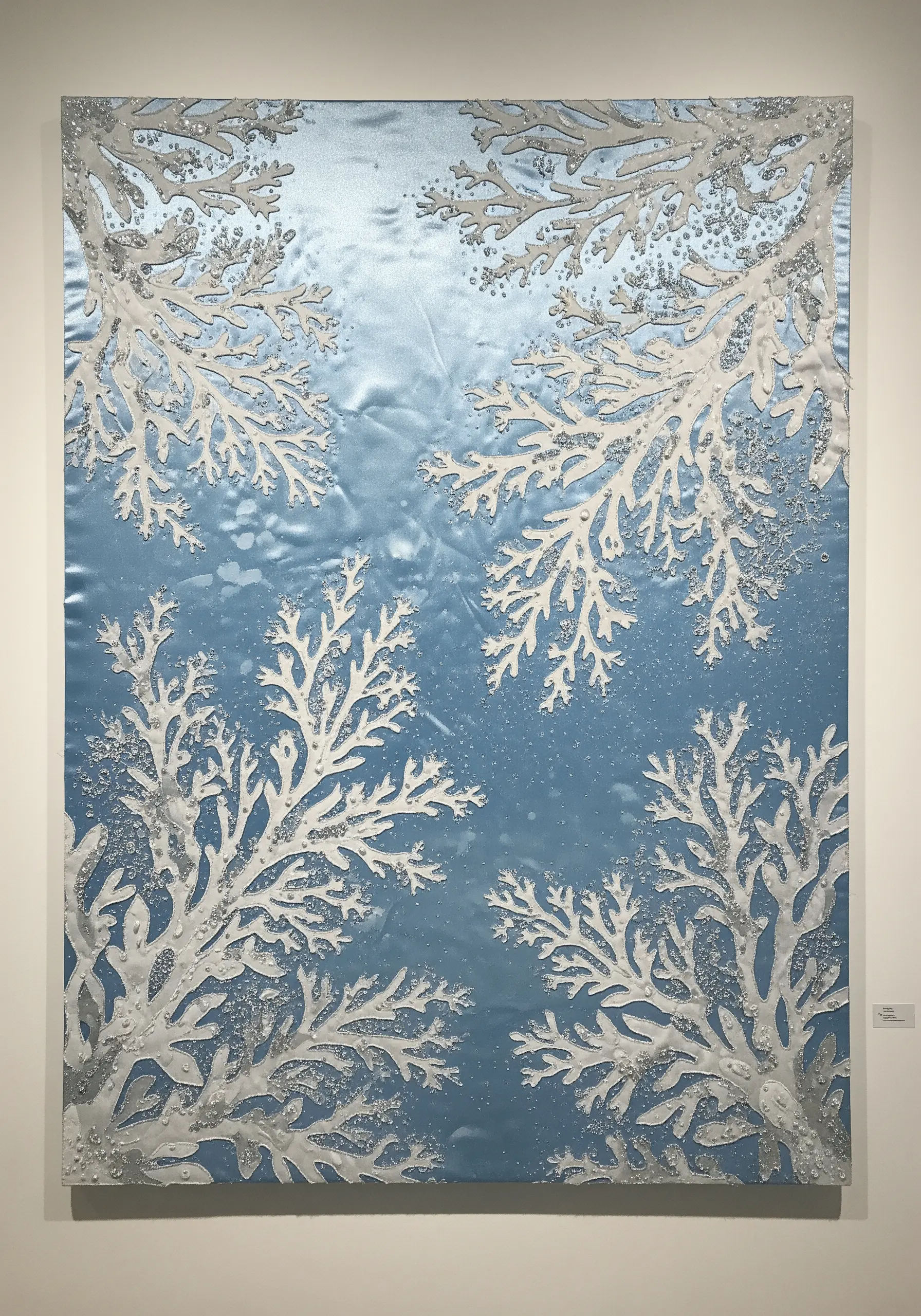 Wall art with white coral shapes on a shimmering blue background, accented with beads for texture.