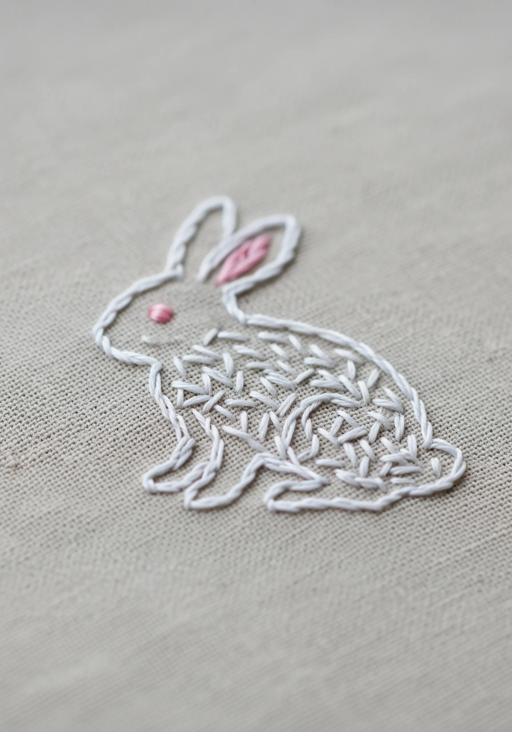 A line art rabbit with a white trellis stitch fill on natural linen fabric.