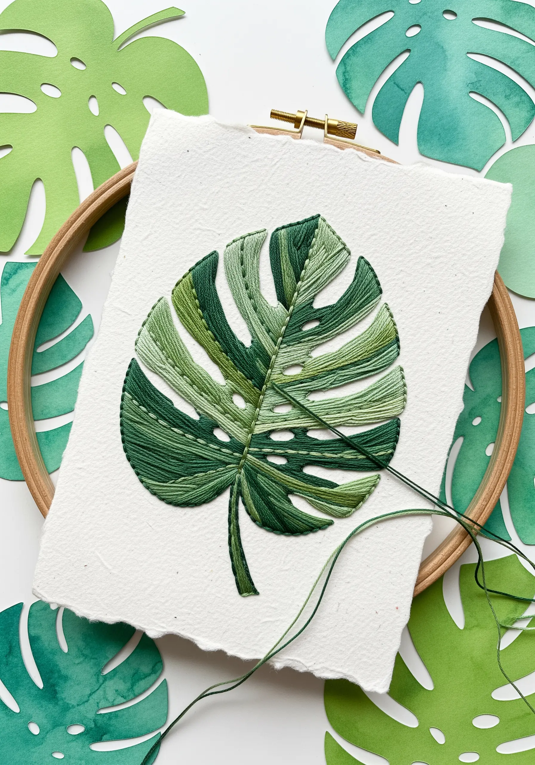 A monstera leaf embroidered with green satin stitch onto thick, deckle-edge white paper.