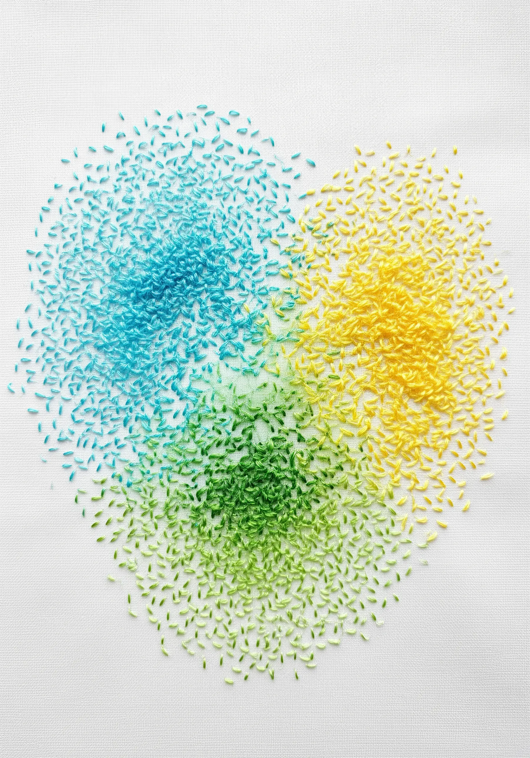 A heart shape made of scattered seed stitches in blue, green, and yellow.
