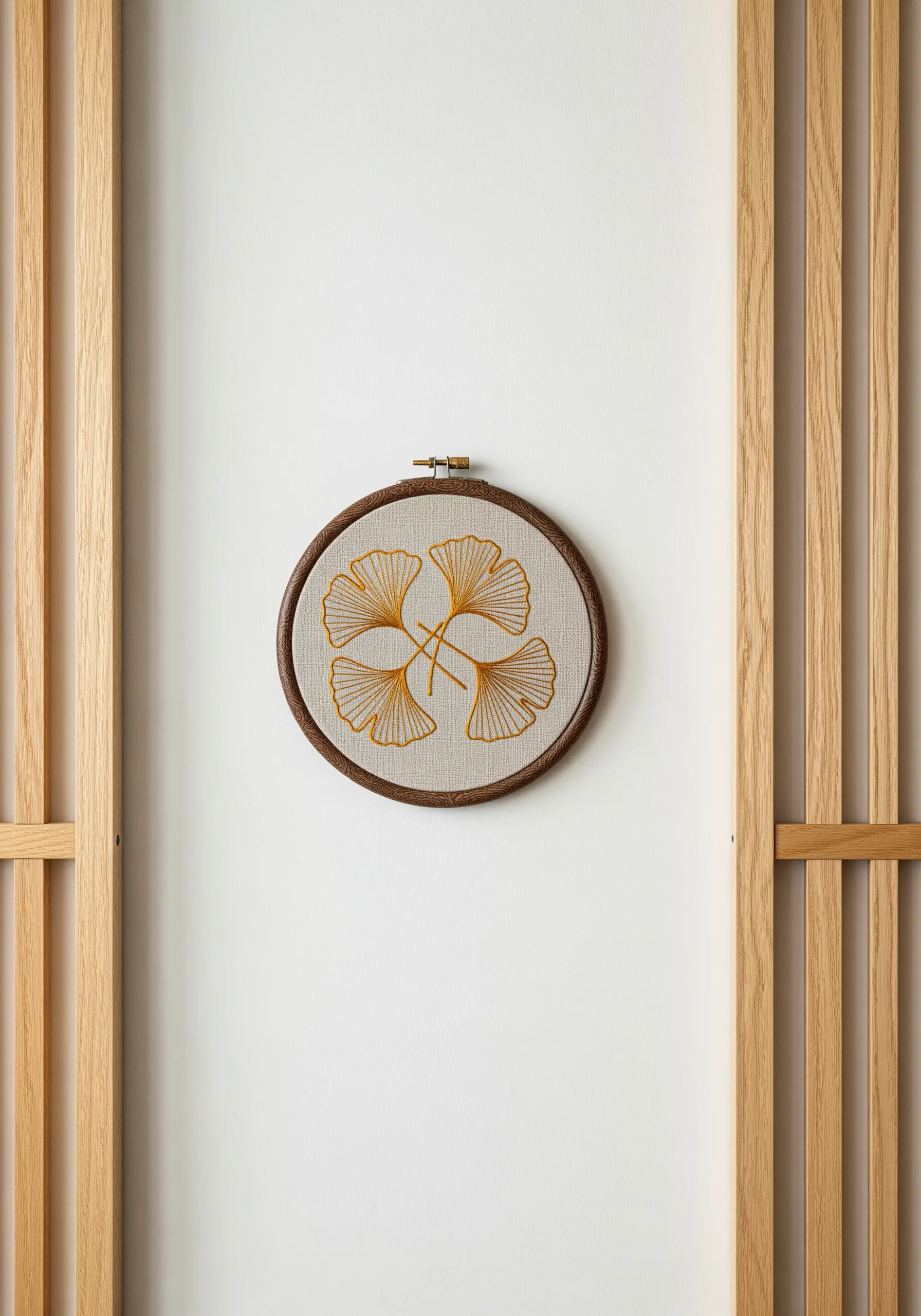 Four embroidered ginkgo leaves with radiating gold stitches in a leather-wrapped hoop.