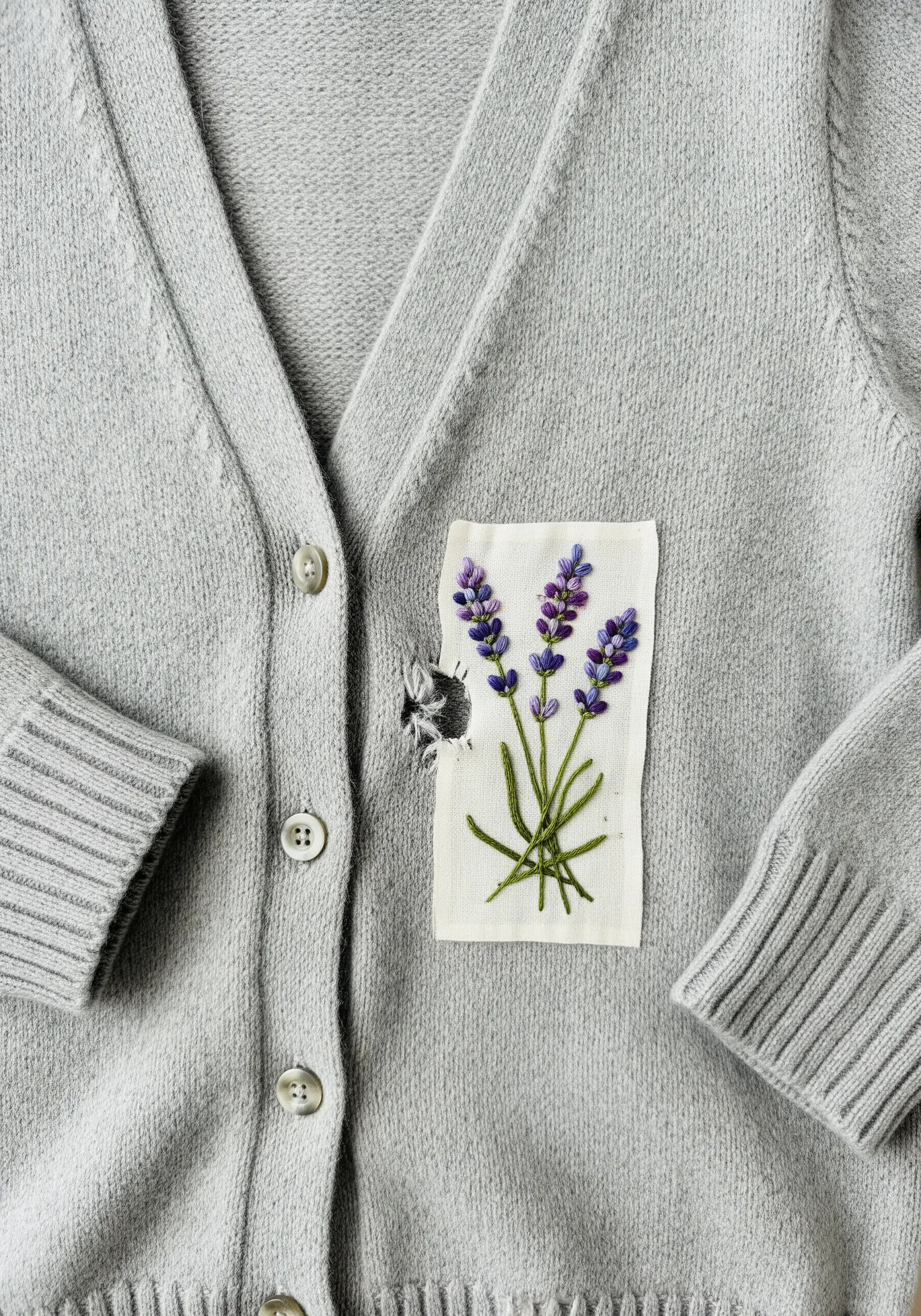 A raw-edge white patch with embroidered lavender covering a hole on a gray cashmere cardigan.