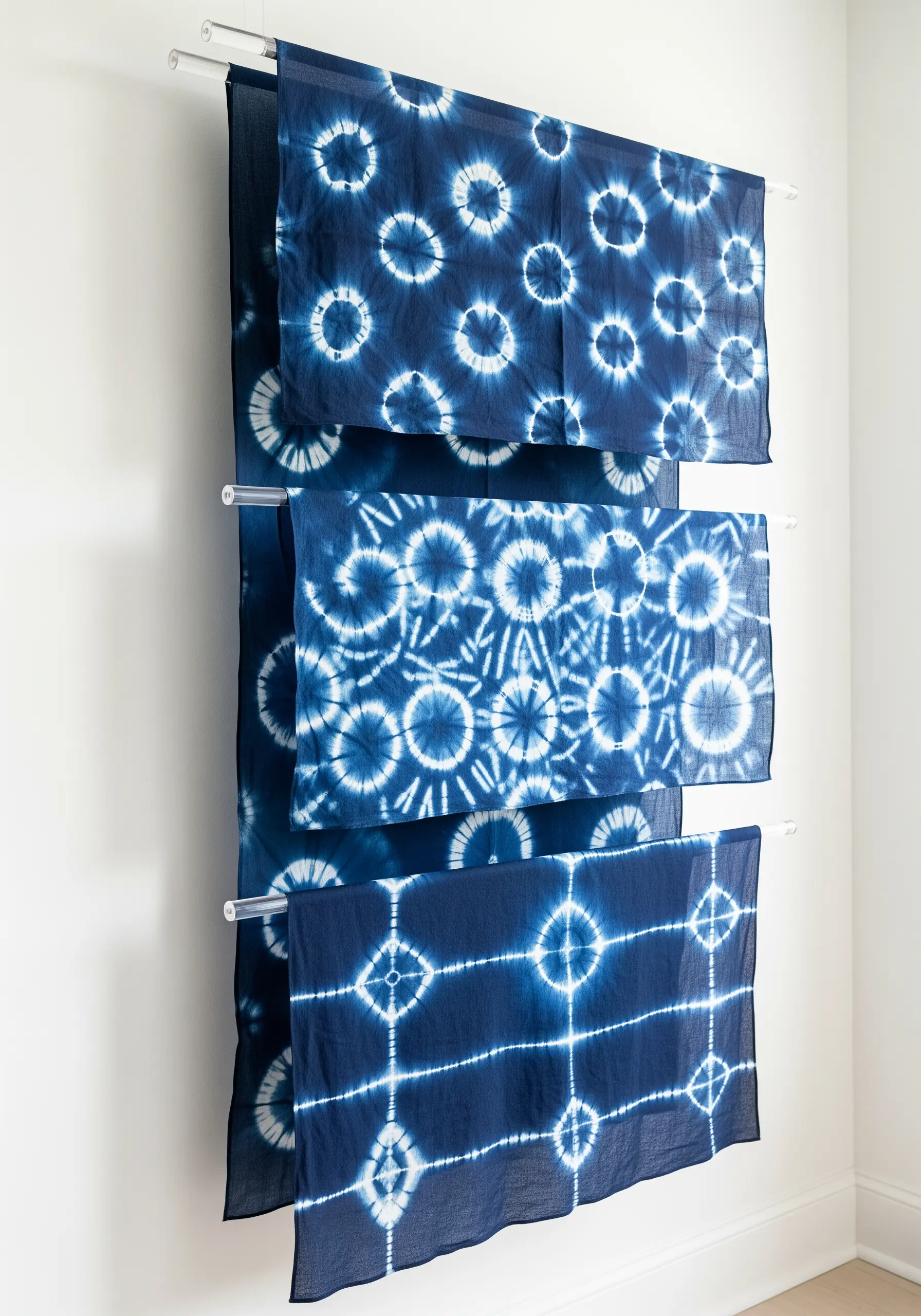 Three pieces of indigo shibori-dyed fabric with different geometric patterns hanging on a white wall.