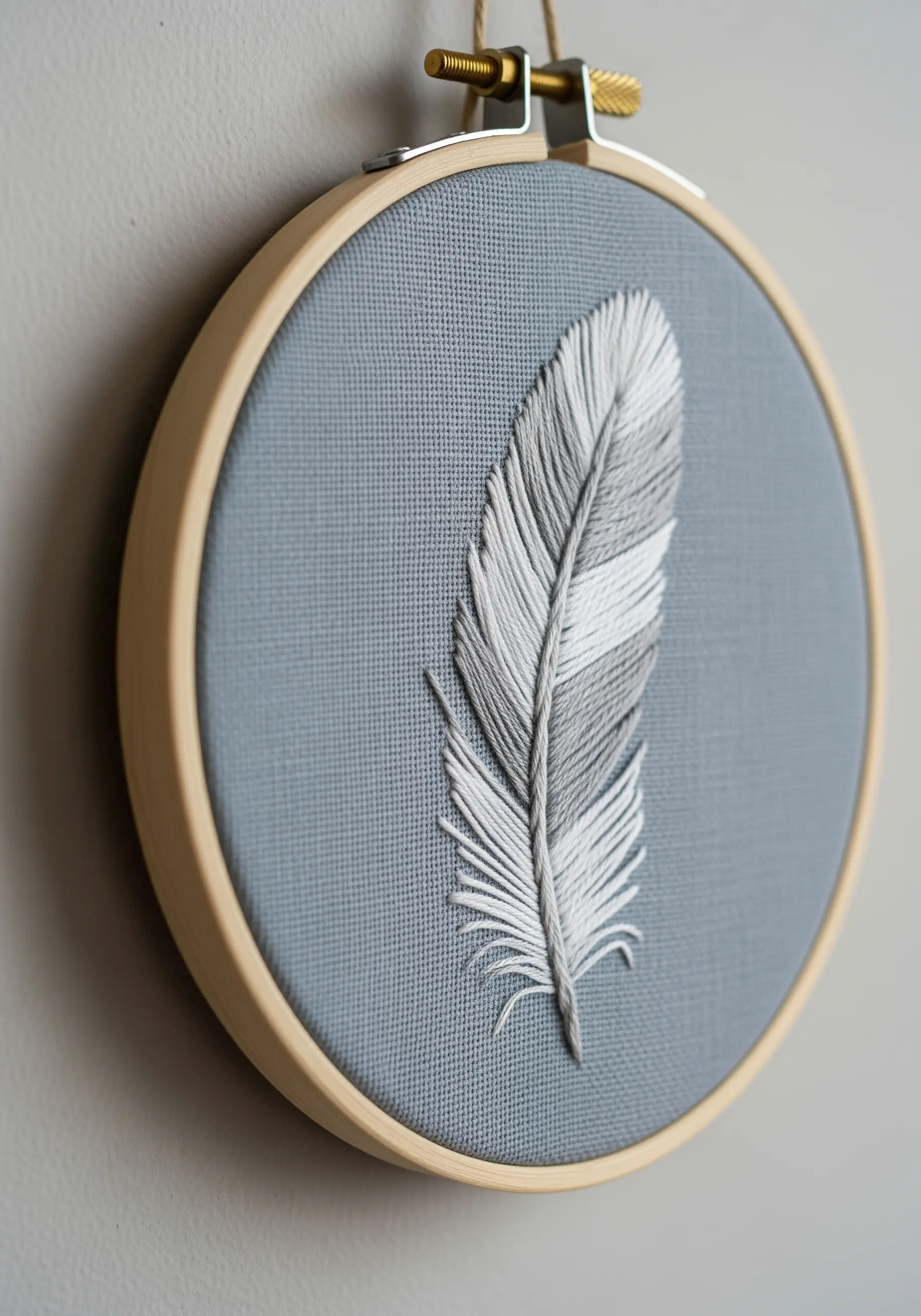 A realistic feather embroidered with angled long-and-short stitch in gray and white.