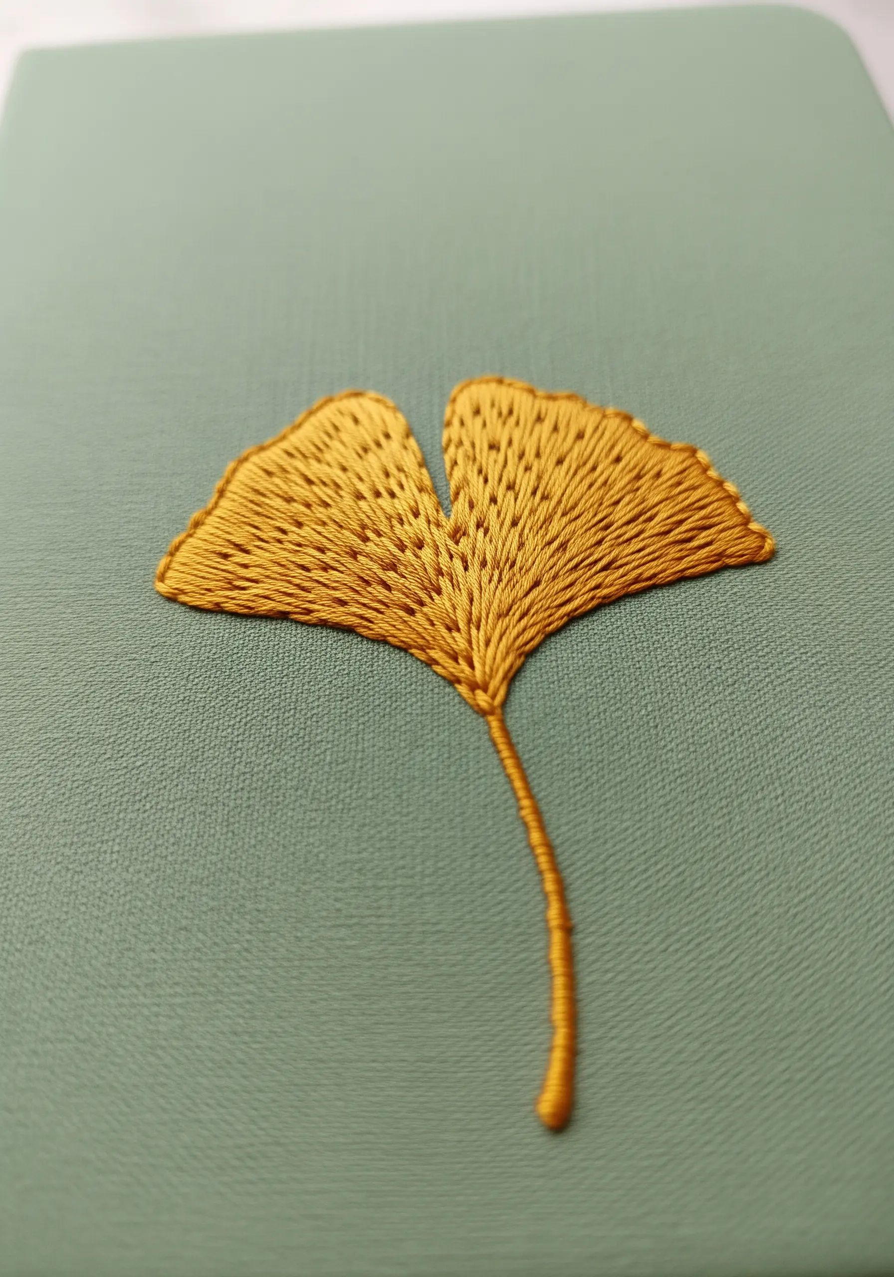 A golden-yellow ginkgo leaf embroidered with satin stitches that radiate from the stem.