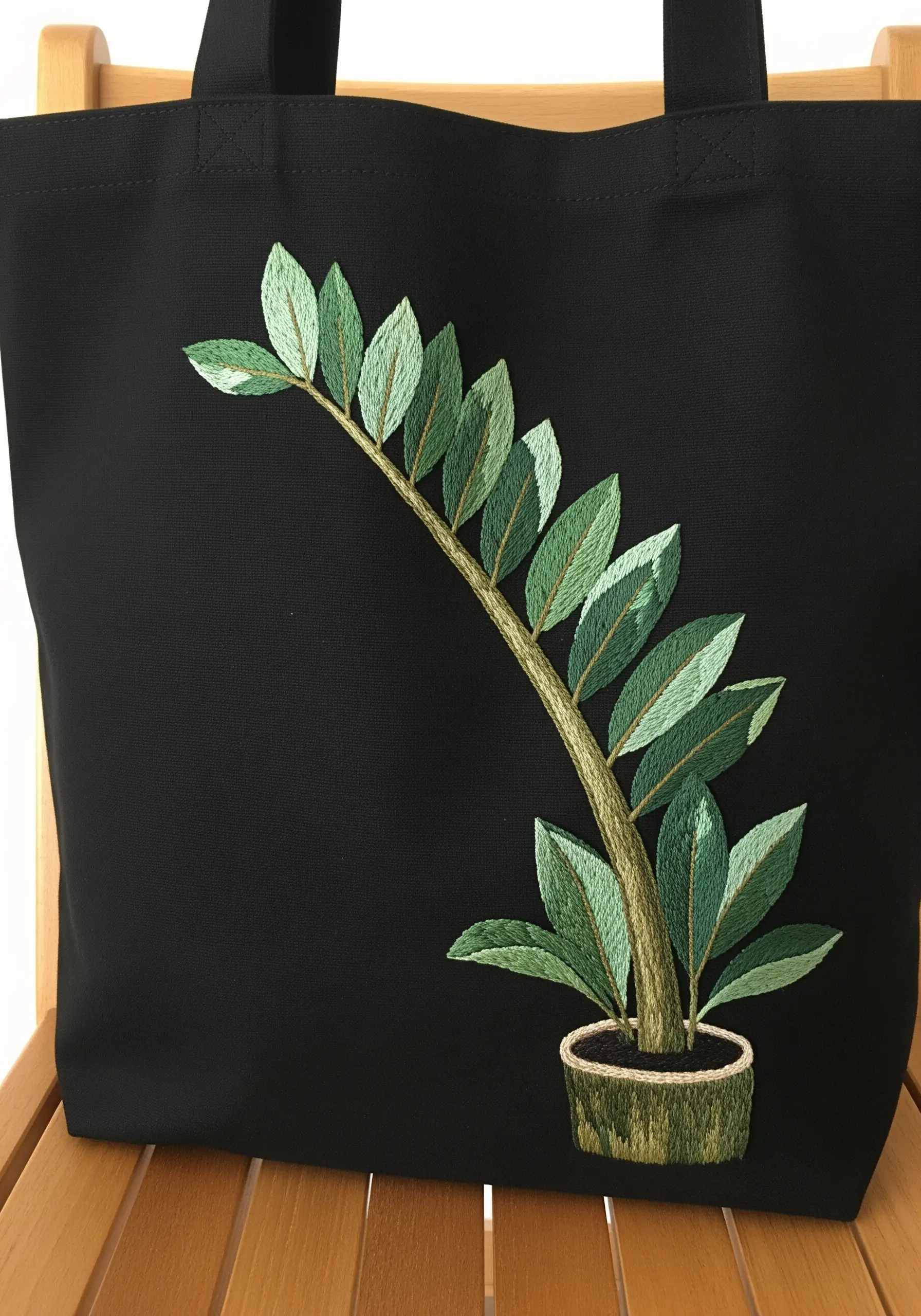 A variegated ZZ plant with carefully angled stitches embroidered on a black tote bag.