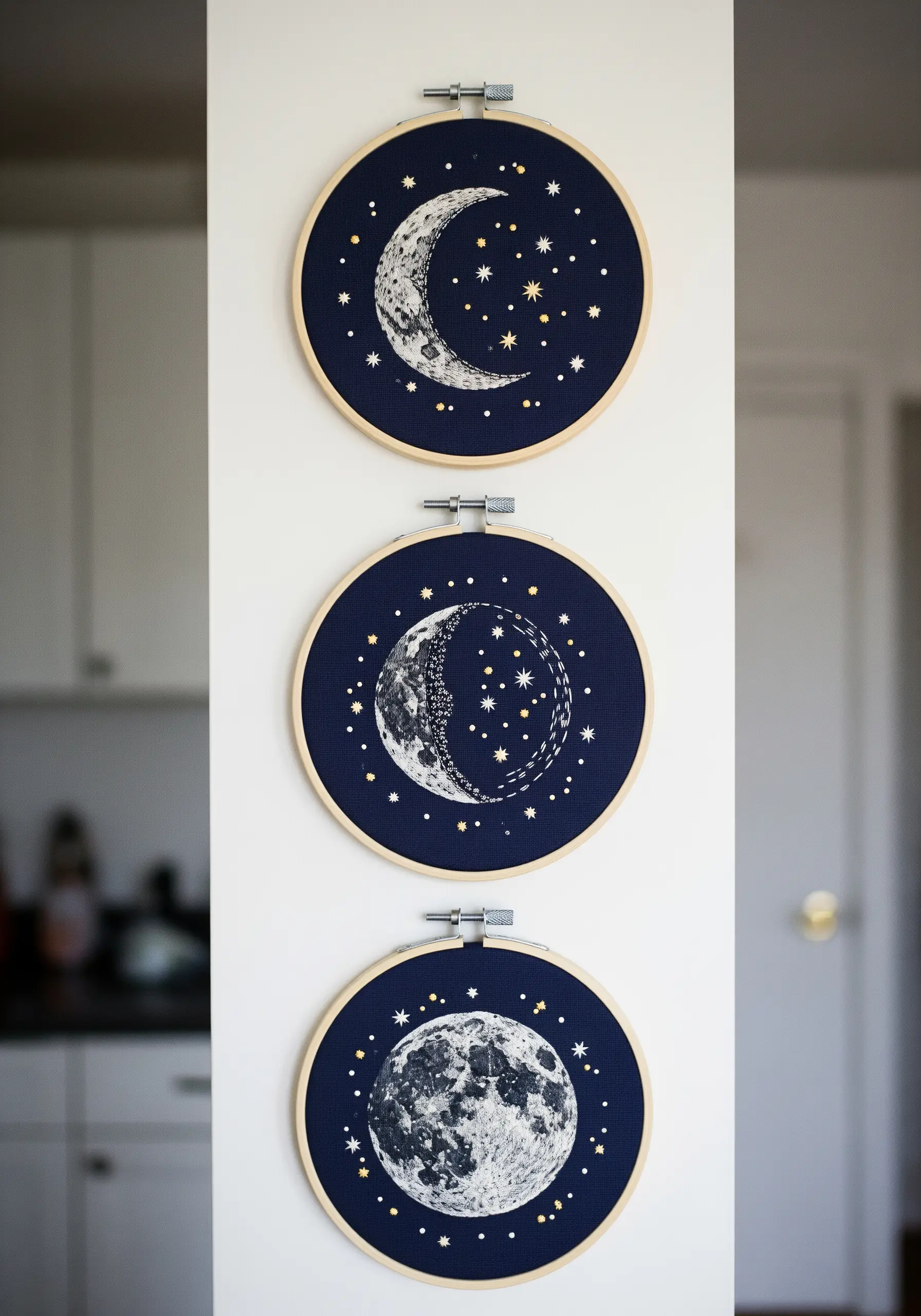 A trio of embroidery hoops showing moon phases against a dark navy background.