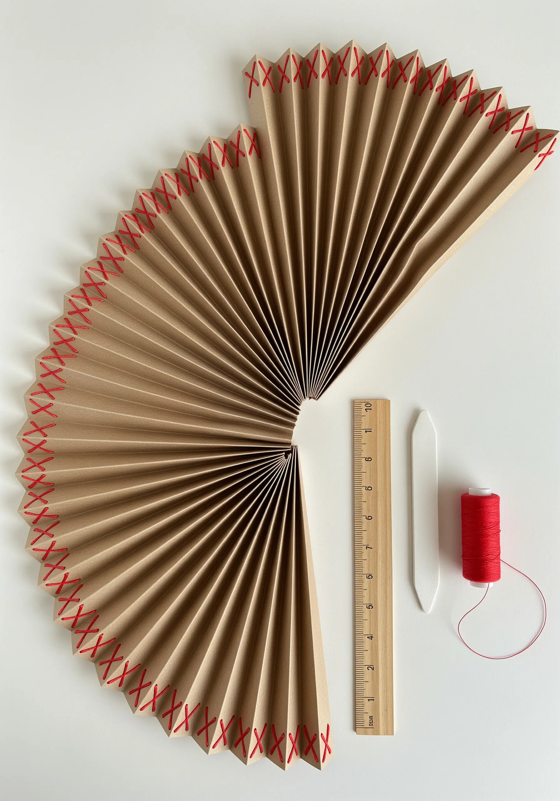 An accordion-folded paper fan with its top edge bound together with red cross-stitches.