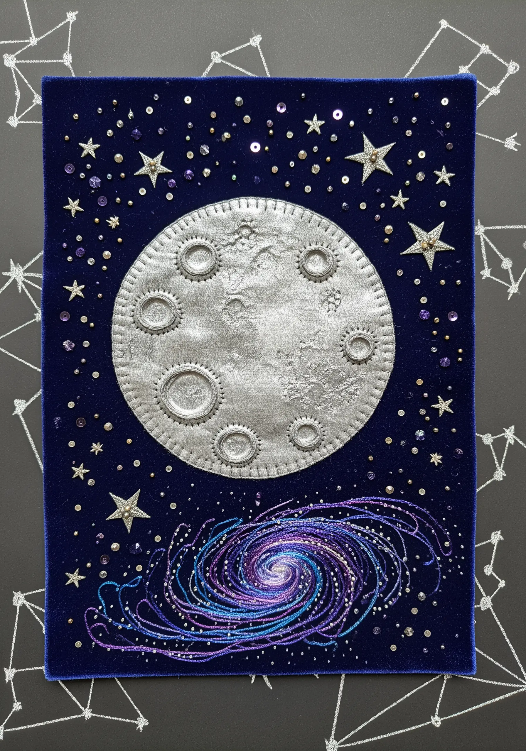 Fabric collage of a moon and galaxy on navy velvet with bead and sequin details