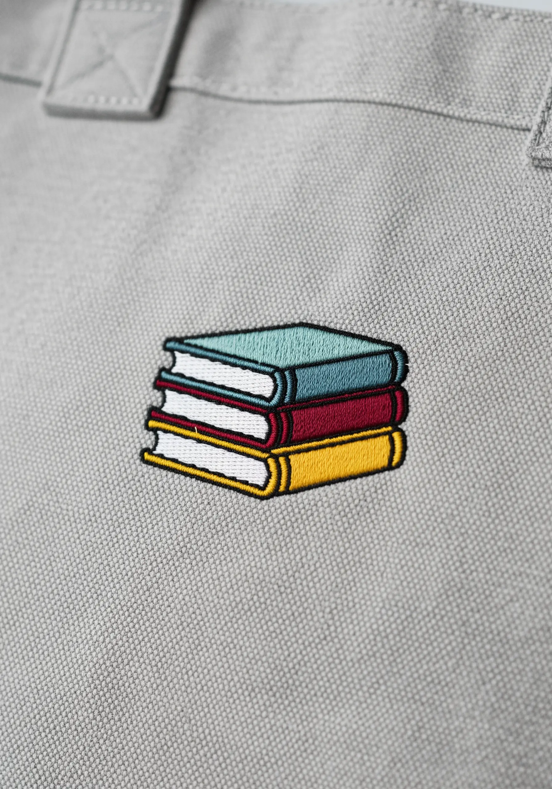A stack of three colorful books with crisp black outlines, embroidered on a tote bag.