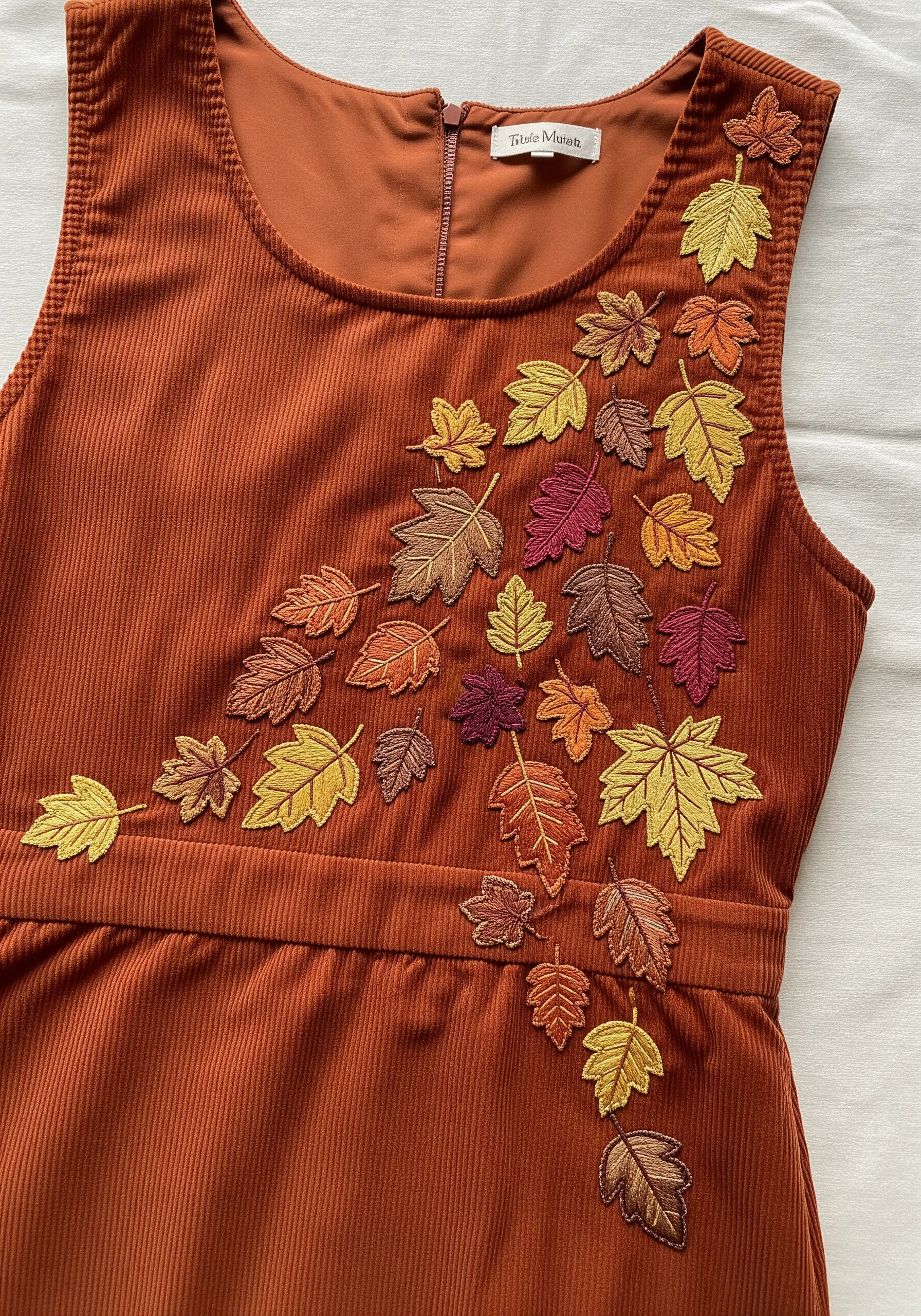 A cascade of autumn leaves in variegated thread on a rust-colored corduroy dress.