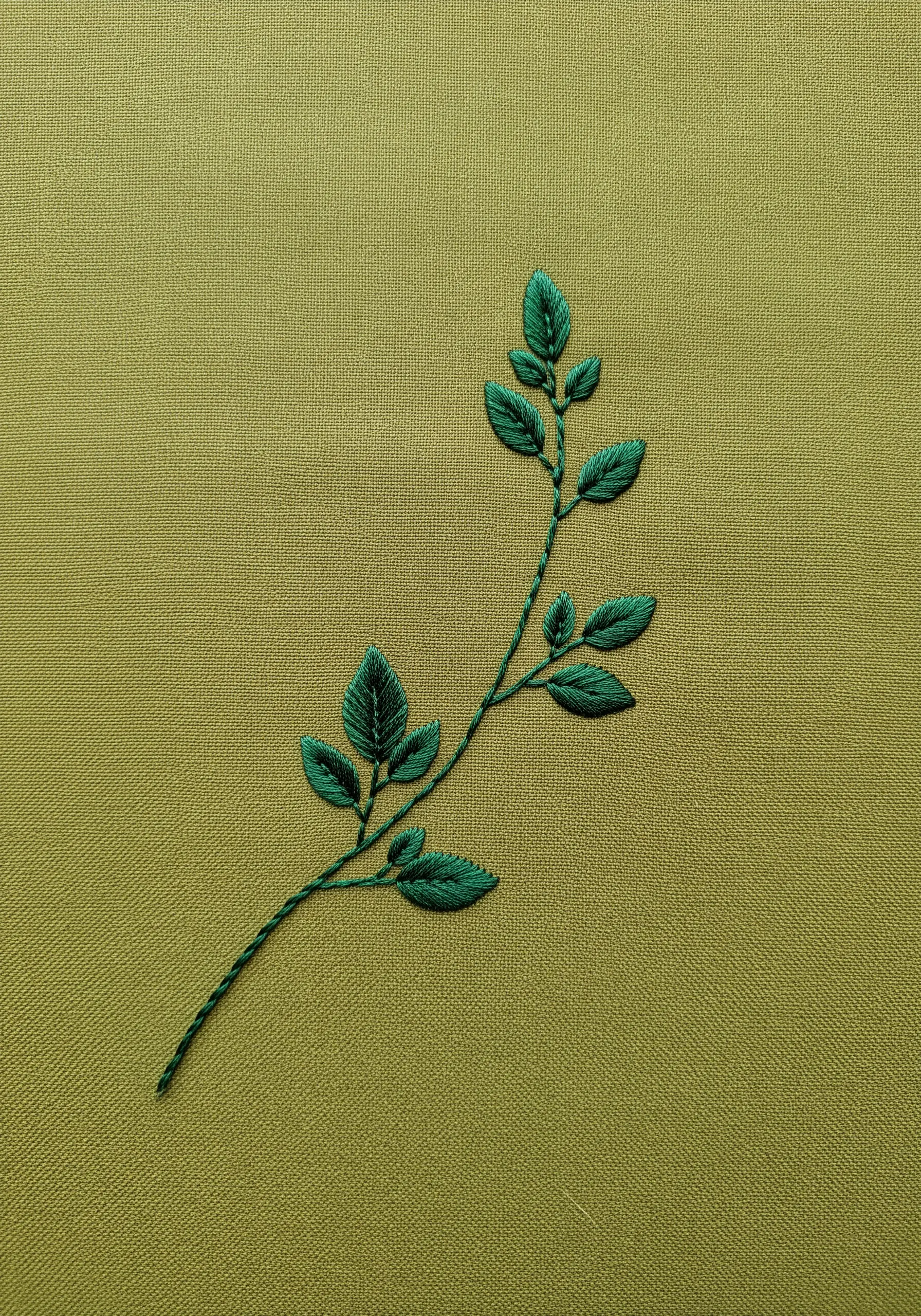A branch with deep green leaves, filled with angled satin stitches to create a central vein.