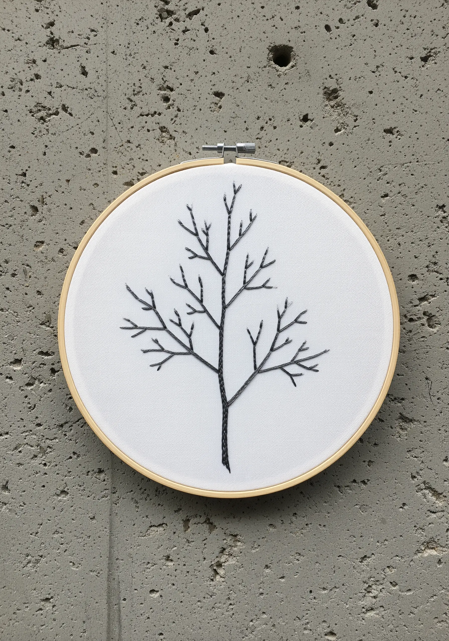 A bare winter tree with a thick trunk and delicate branches stitched in black thread.