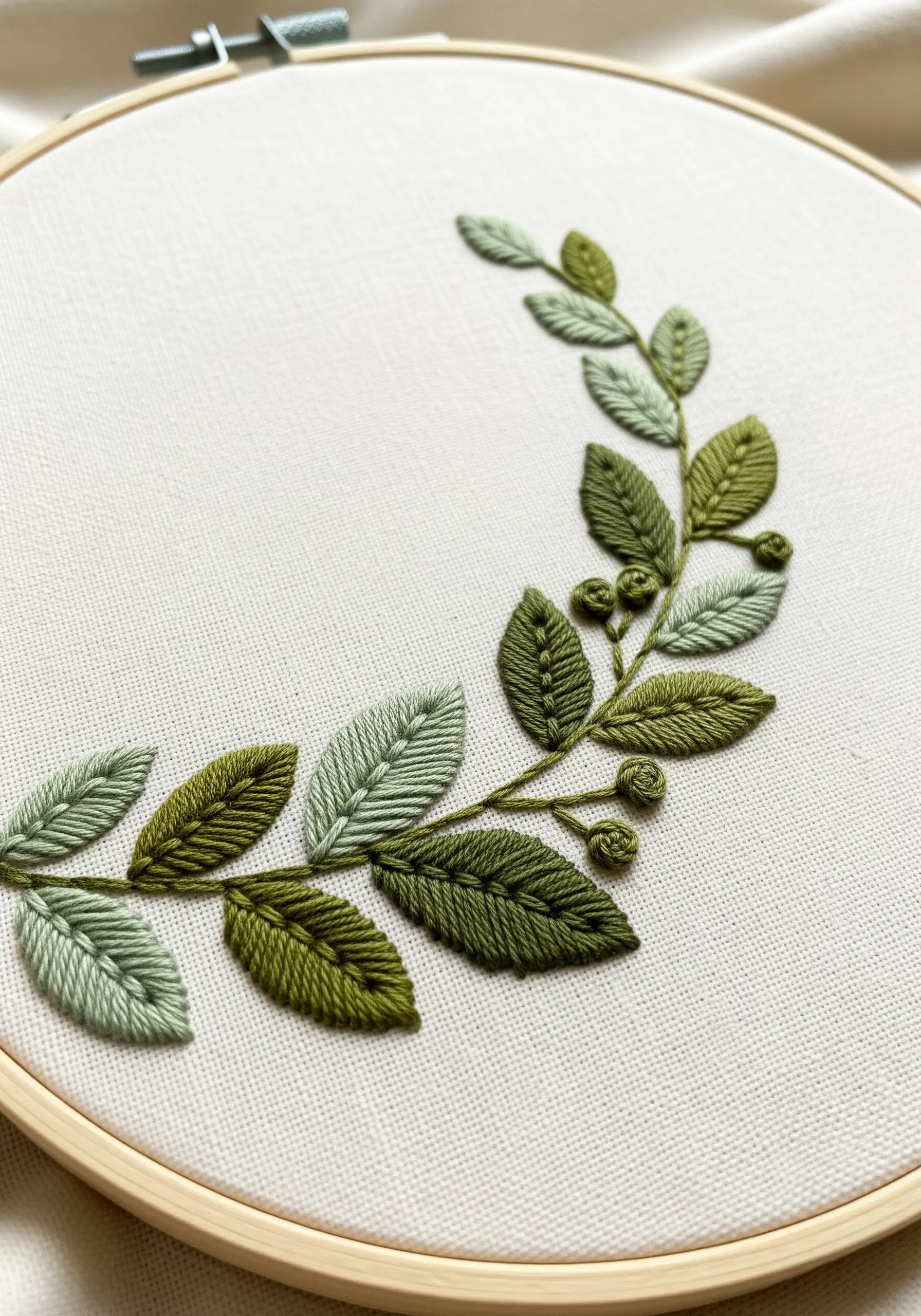 Detail of an embroidered wreath with satin stitch and fishbone stitch leaves.