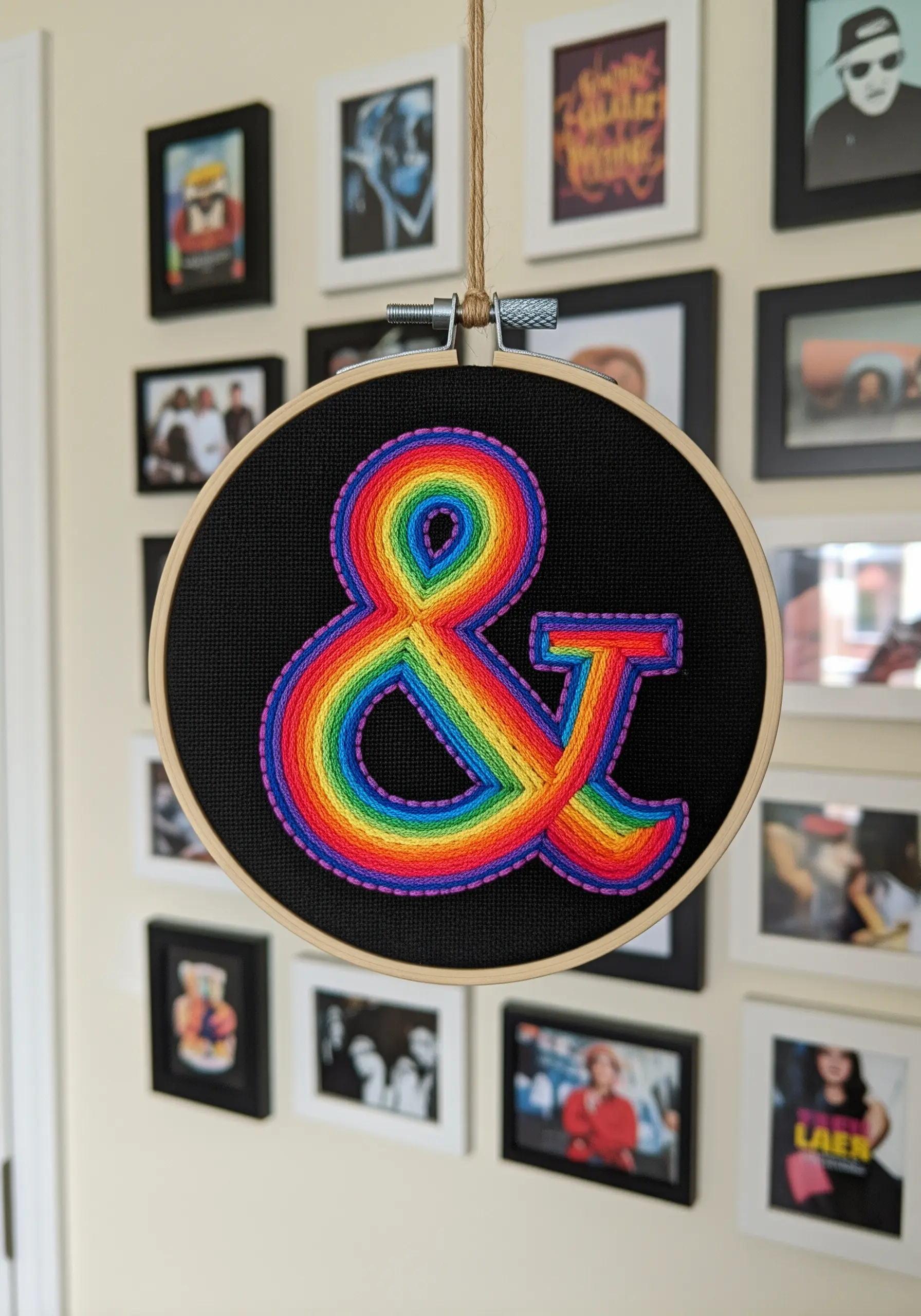 A vibrant rainbow ampersand filled with concentric rows of satin stitch on black fabric.