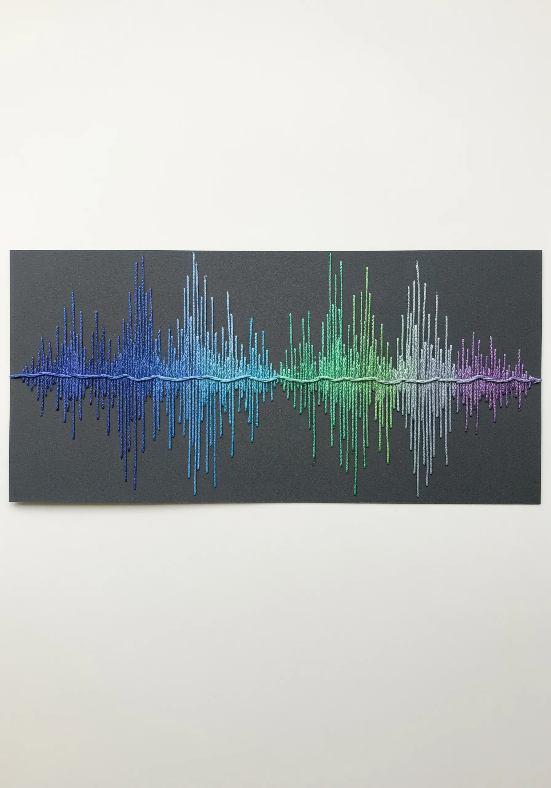 A soundwave embroidered on black paper with a colorful gradient of thread creating the peaks.