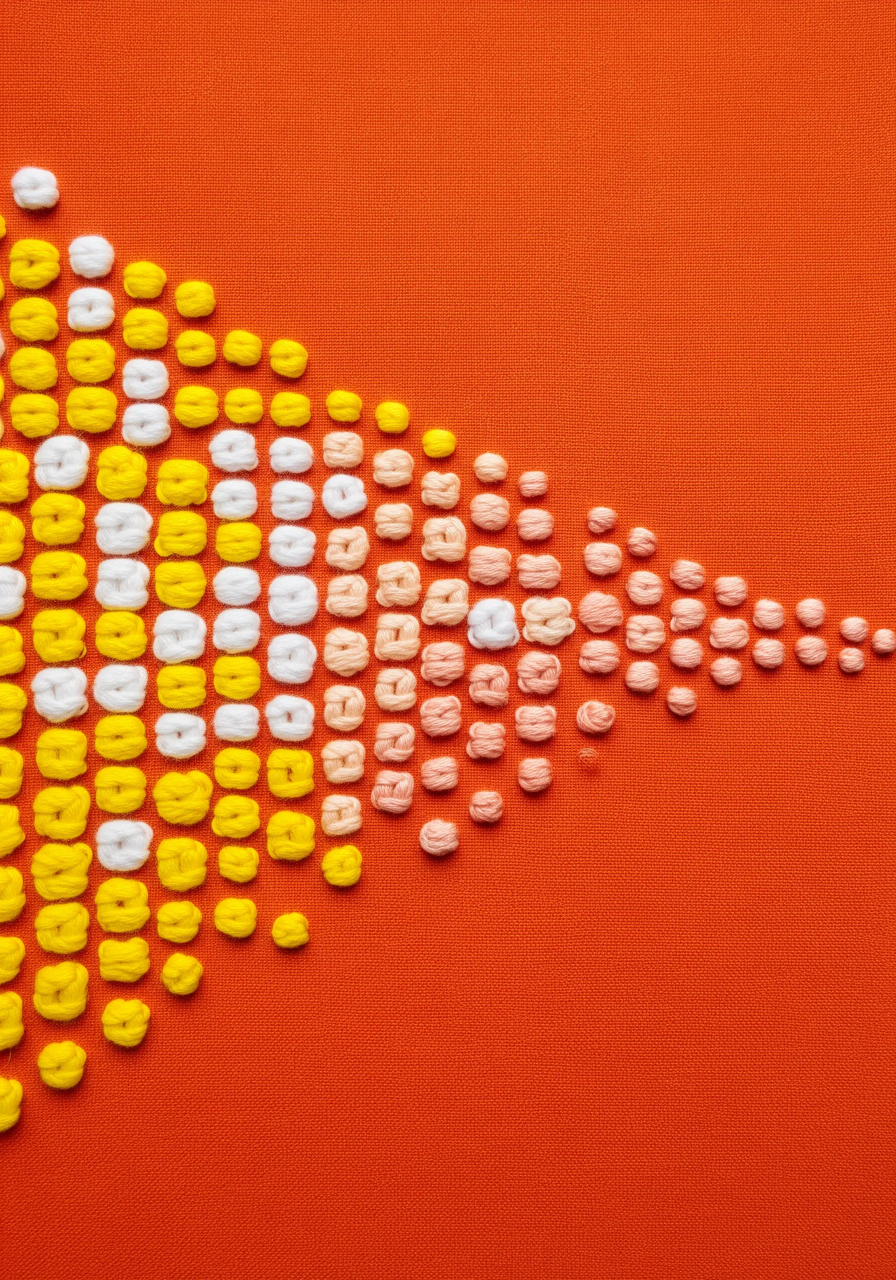 A pattern of yellow, white, and peach French knots on orange fabric, forming a tapering shape.