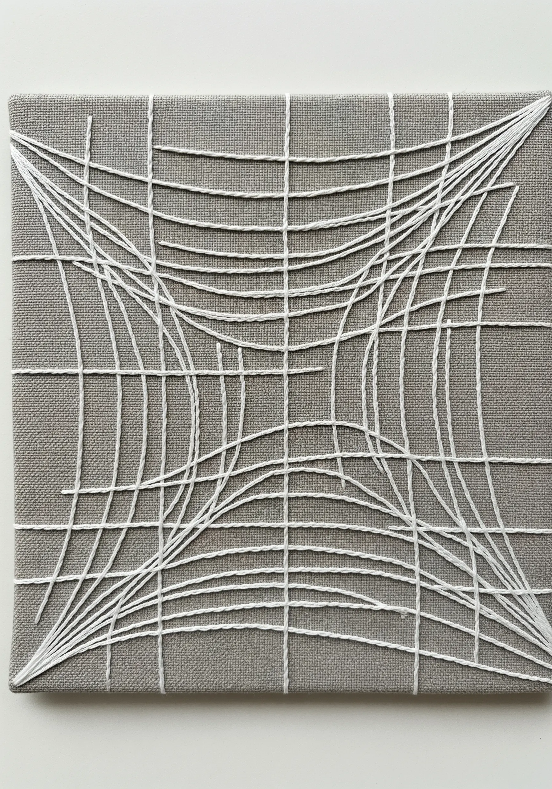 A string art embroidery piece showing a white grid distorted into a 3D optical illusion on gray canvas.