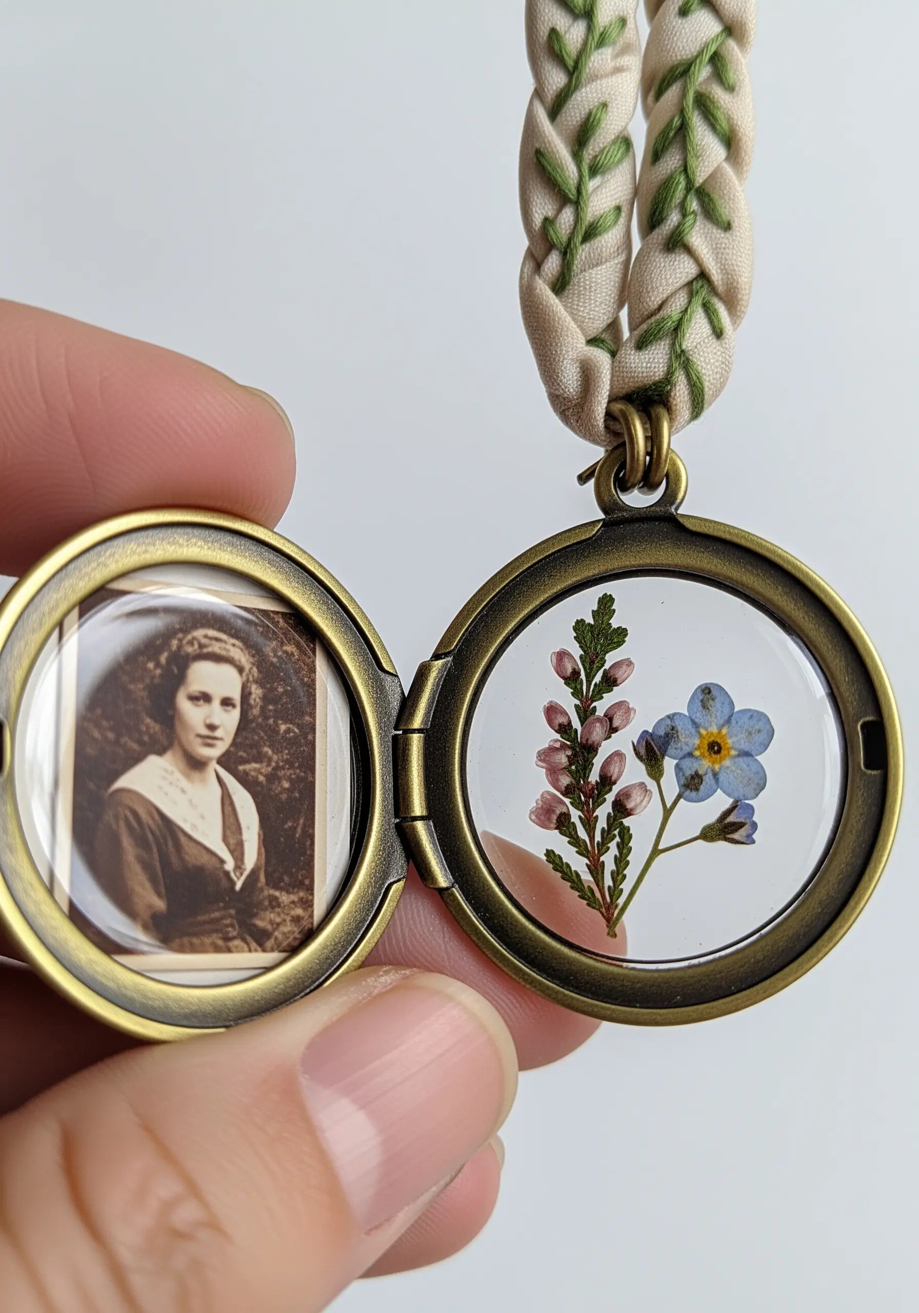 A vintage-style locket with pressed flowers on one side and an old photo on the other.