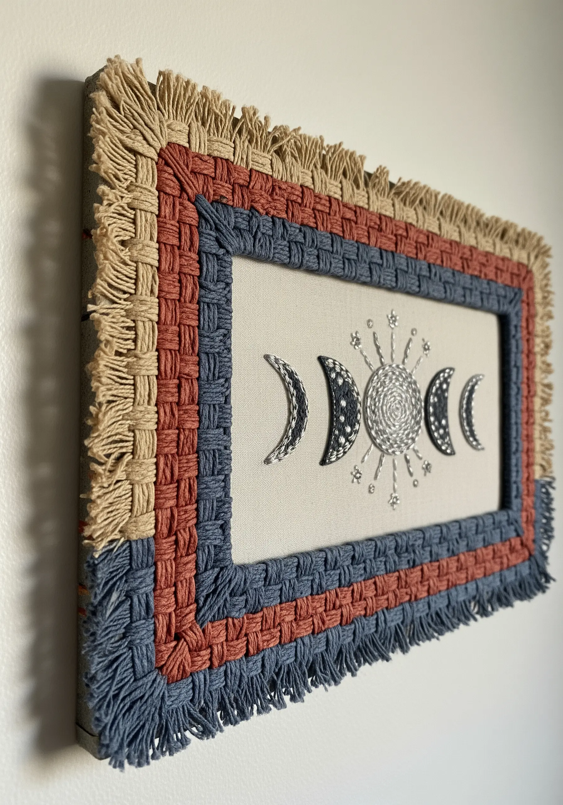 Celestial moon phase embroidery with a woven yarn and macrame fringe border.