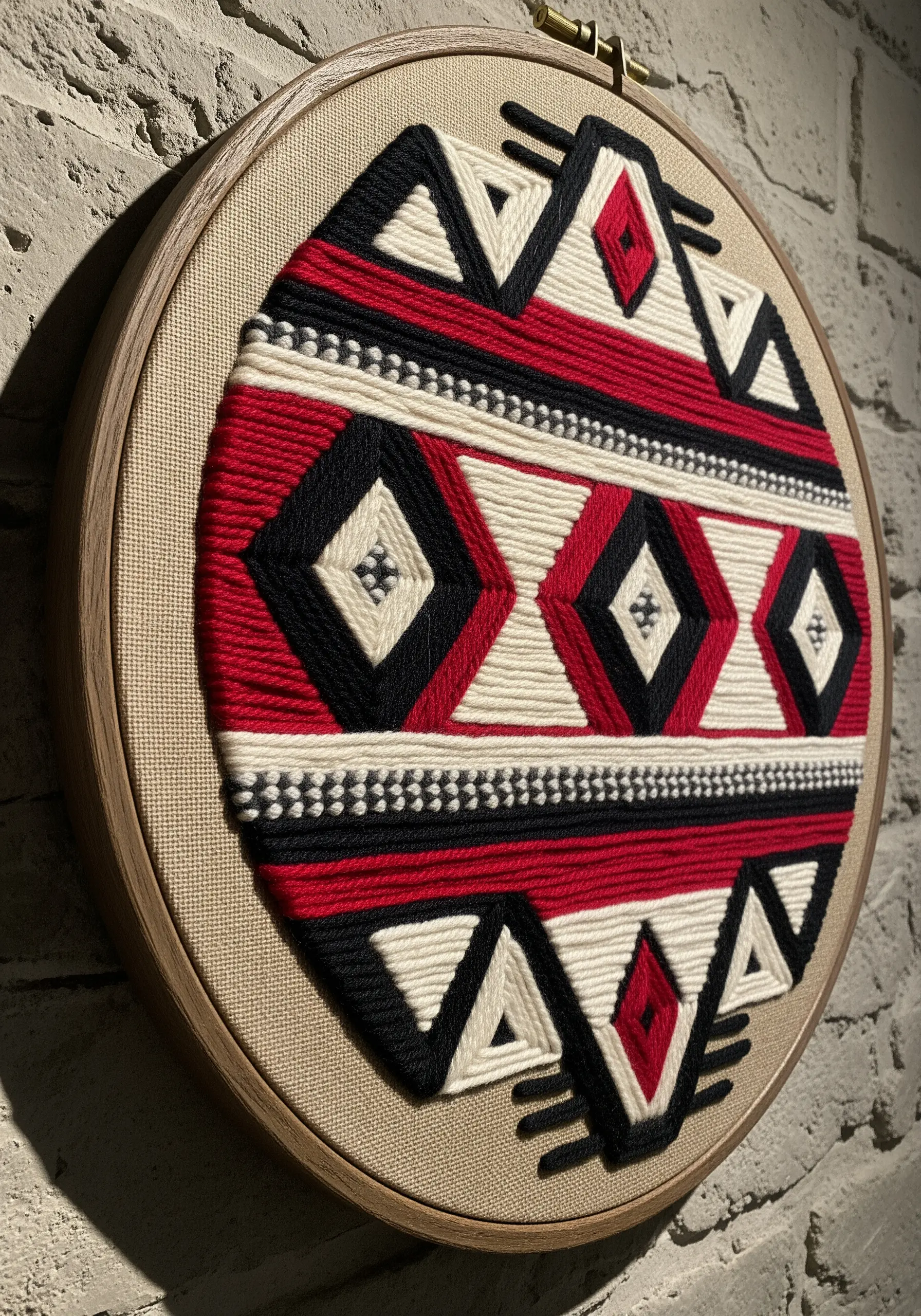 A woven tapestry with a red, black, and white geometric pattern made inside an embroidery hoop.