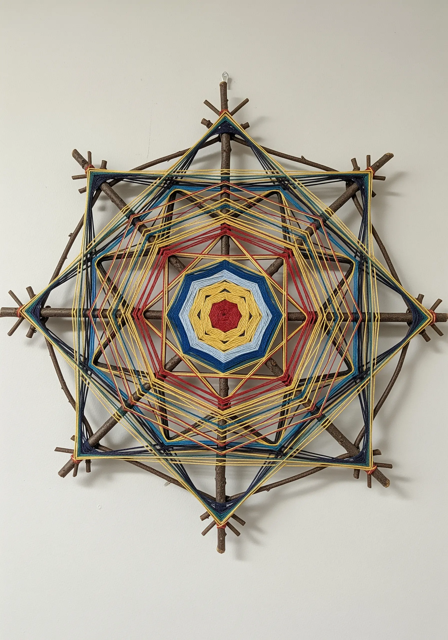 A geometric 'Ojo de Dios' weaving made with colorful yarn wrapped around a frame of twigs.