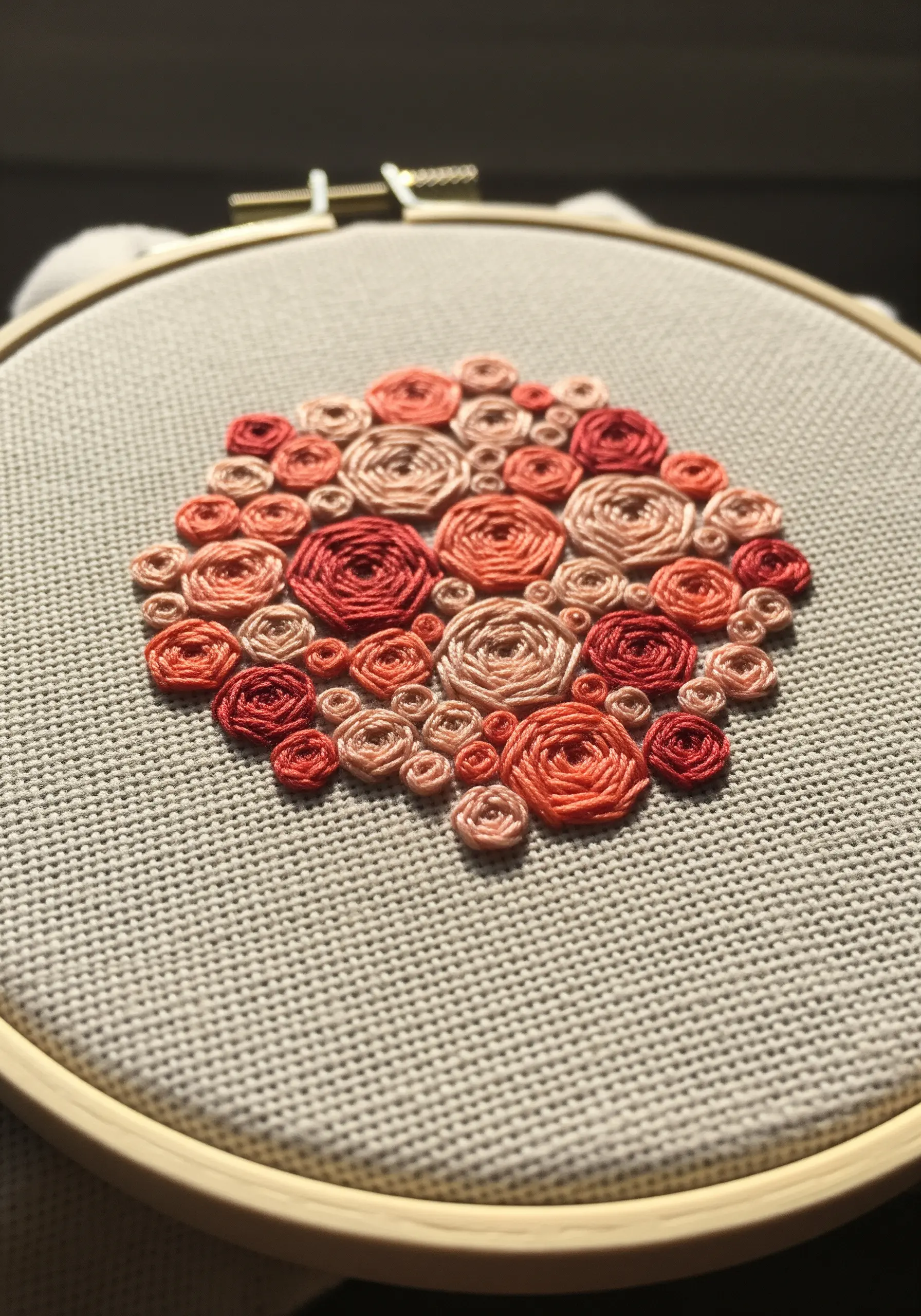 A cluster of woven wheel roses in shades of pink, red, and coral on neutral fabric.