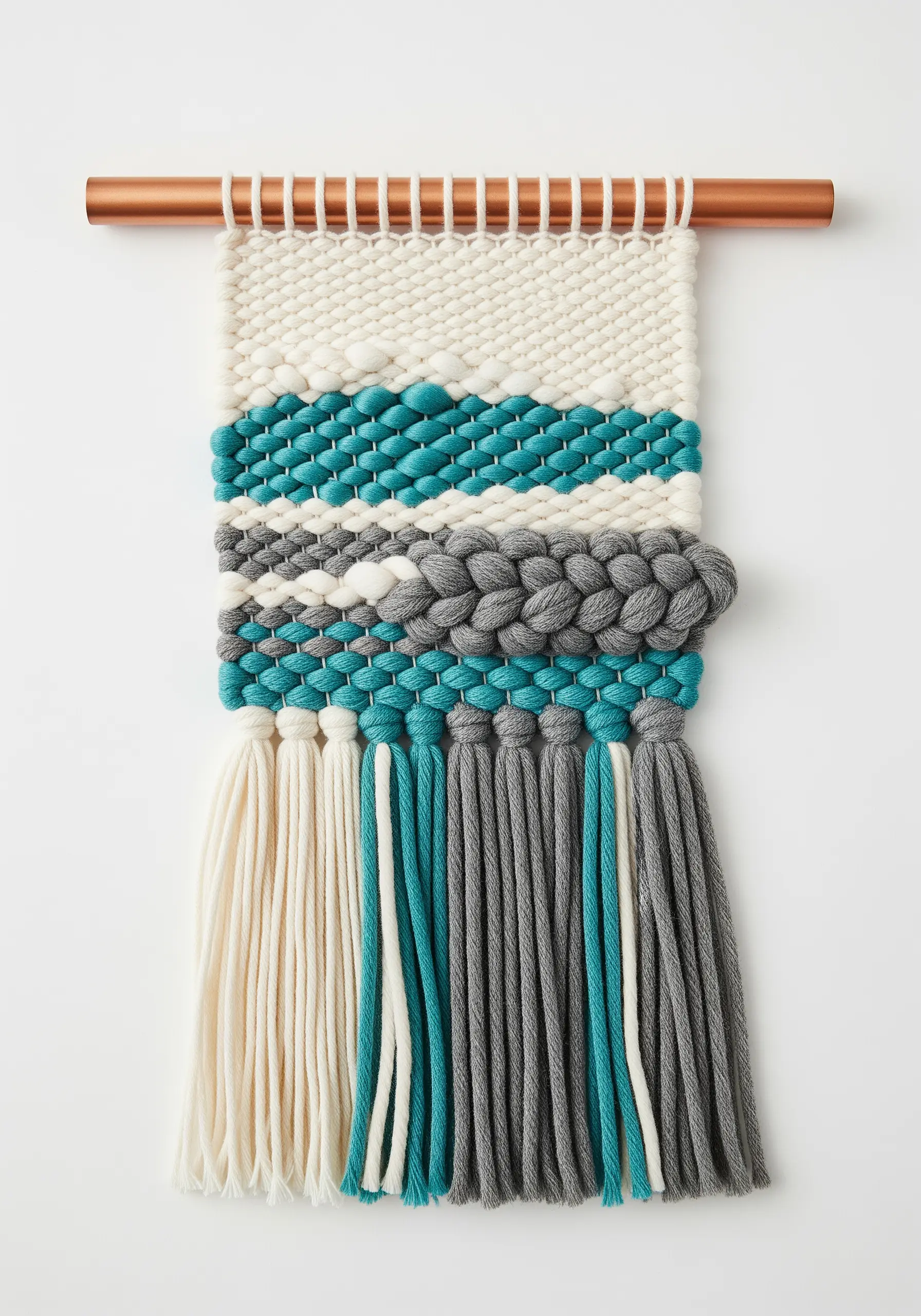 A woven wall hanging with sections of different textures in teal, grey, and cream yarn.