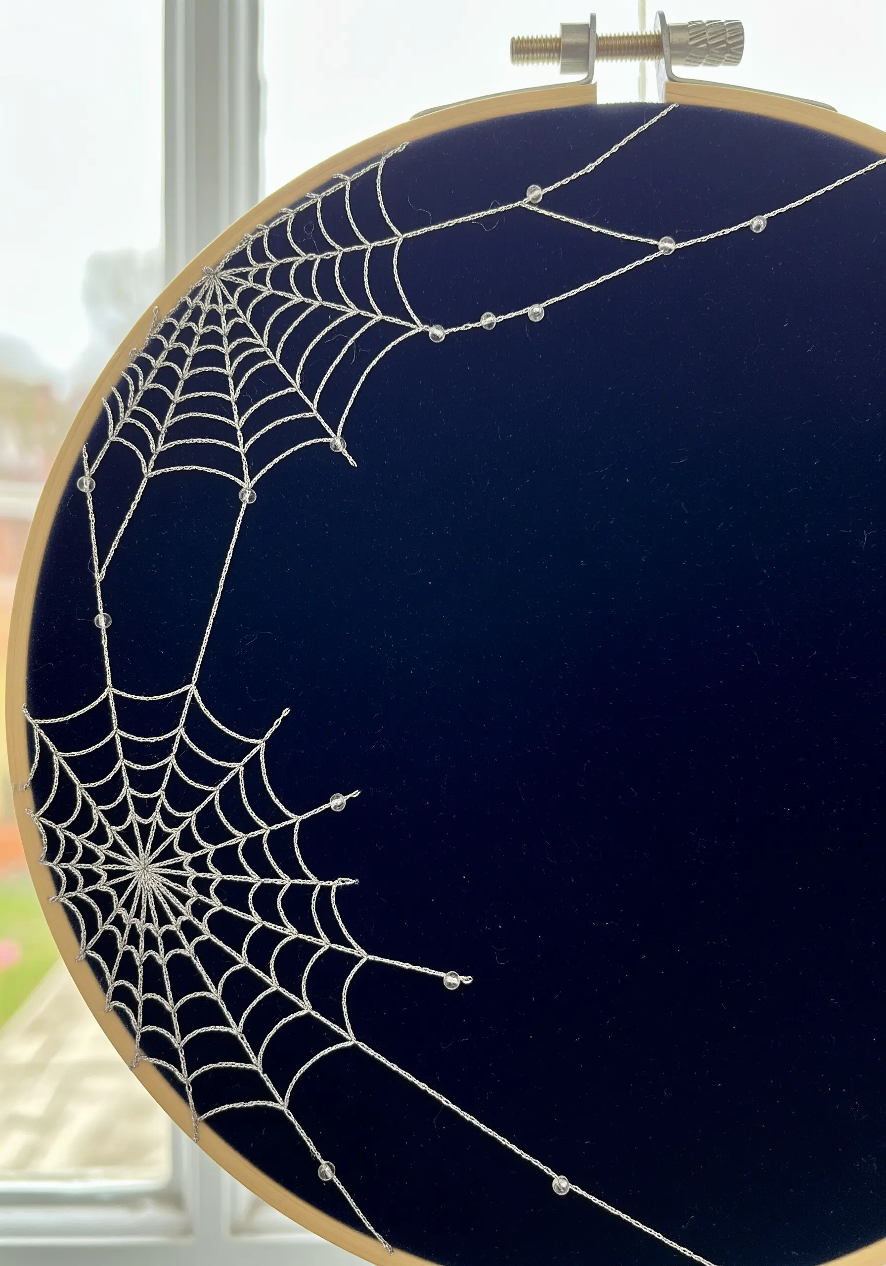 A delicate spiderweb embroidered with silver metallic thread and tiny beads on dark blue velvet.