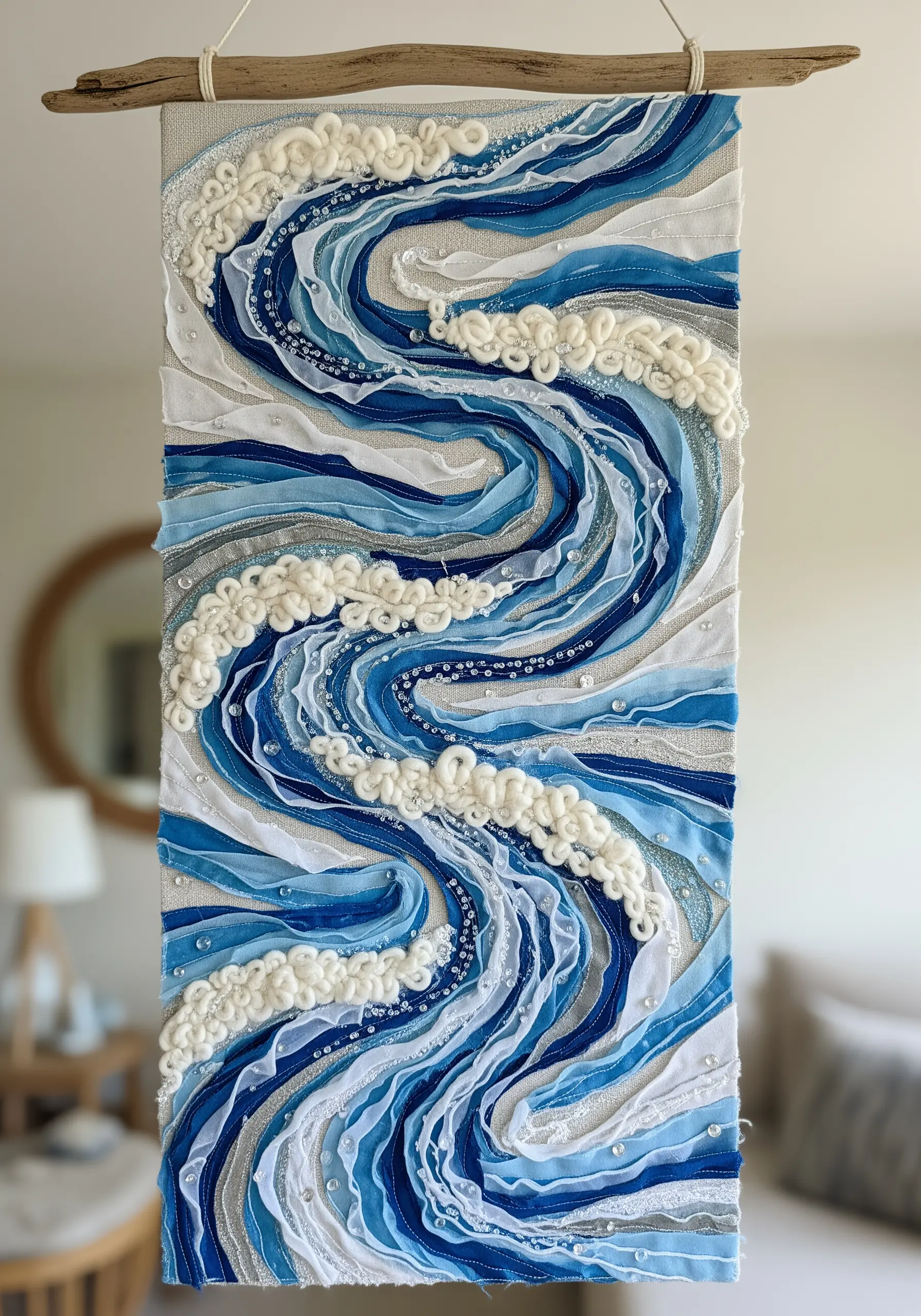 A textured wall hanging of ocean waves made with layered blue sheer ribbons and white yarn knots.