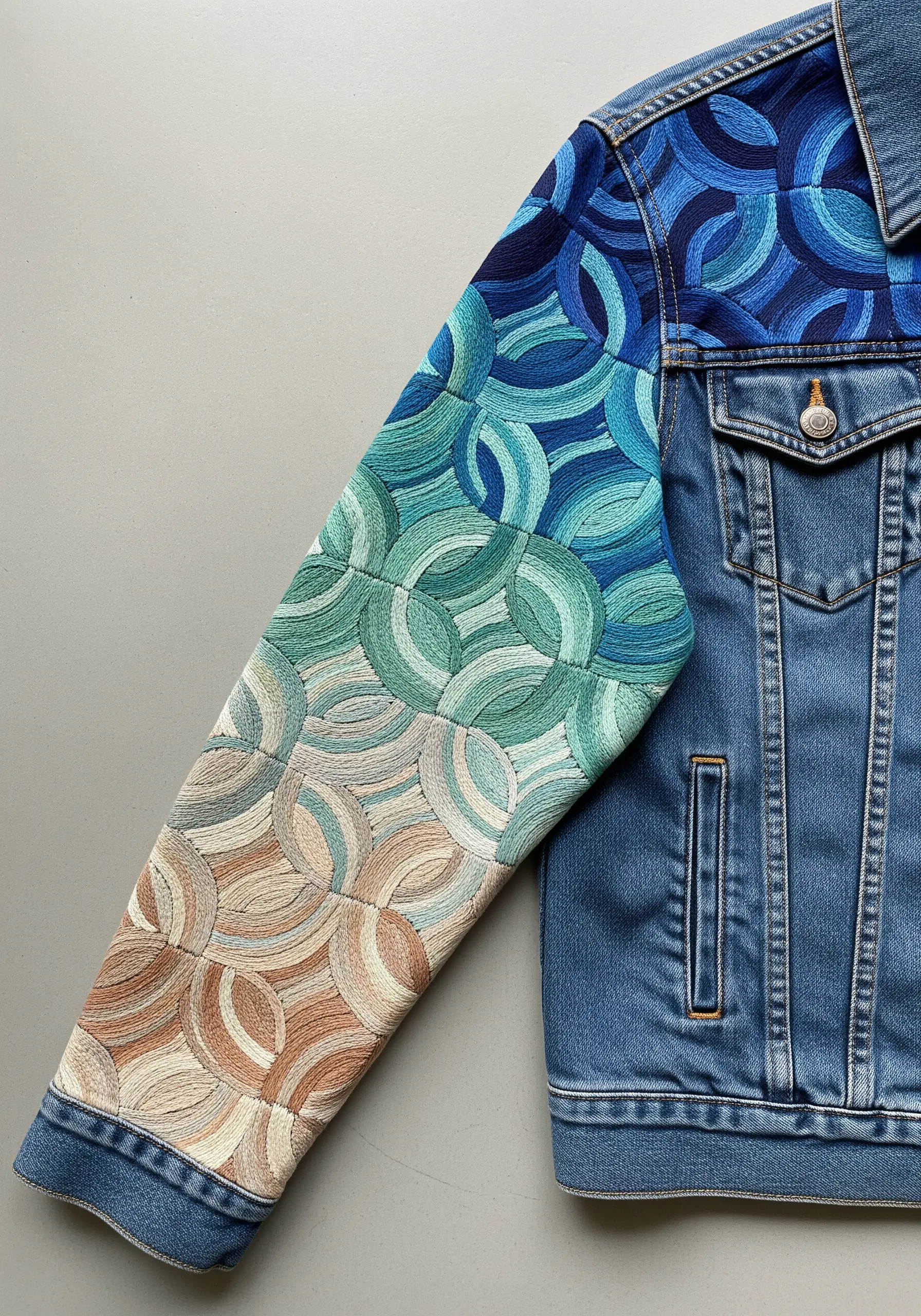 A full sleeve of interlocking circular patterns embroidered in a gradient from blue to beige.