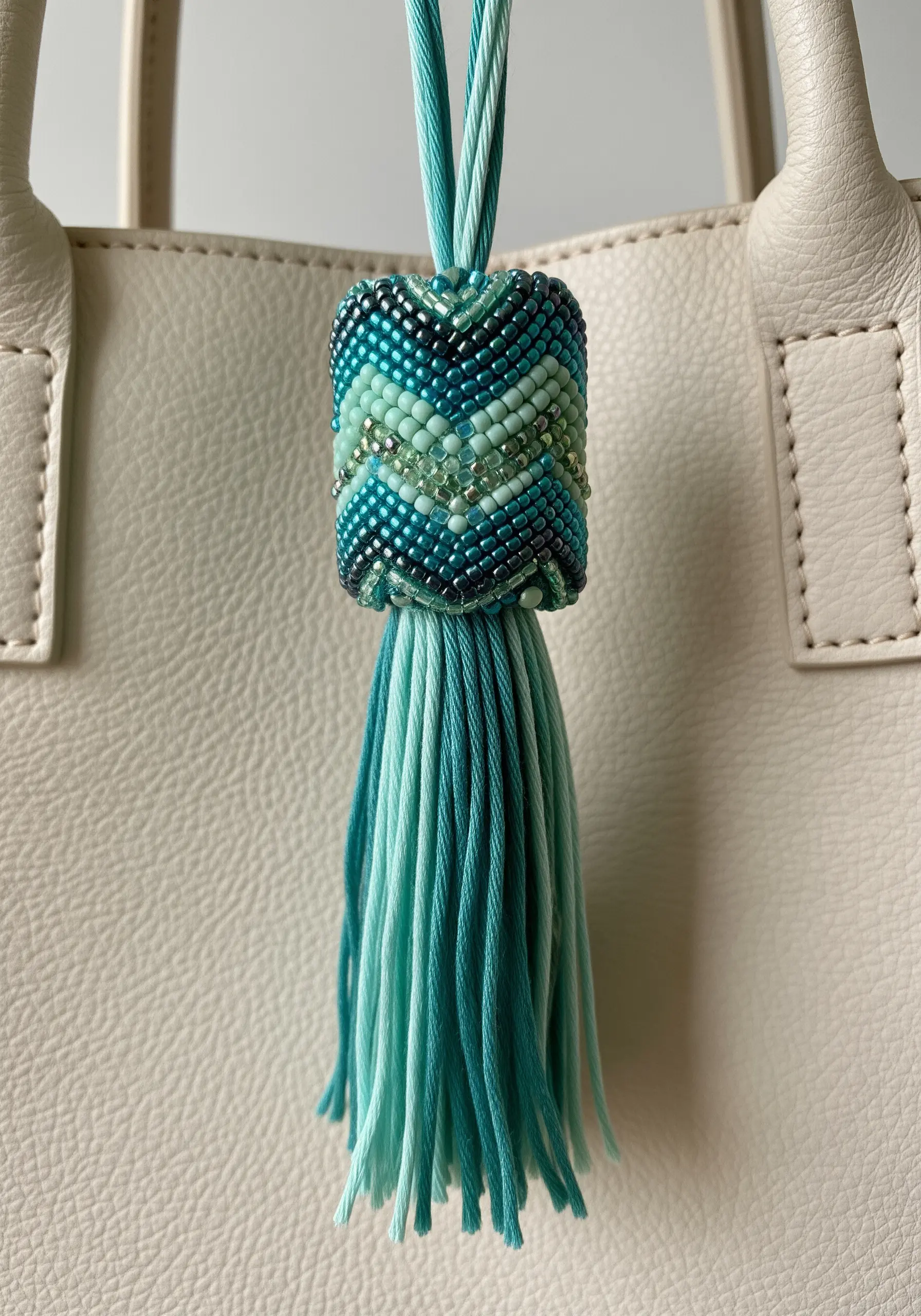 A detailed bag charm with a woven beaded top and a two-tone tassel.
