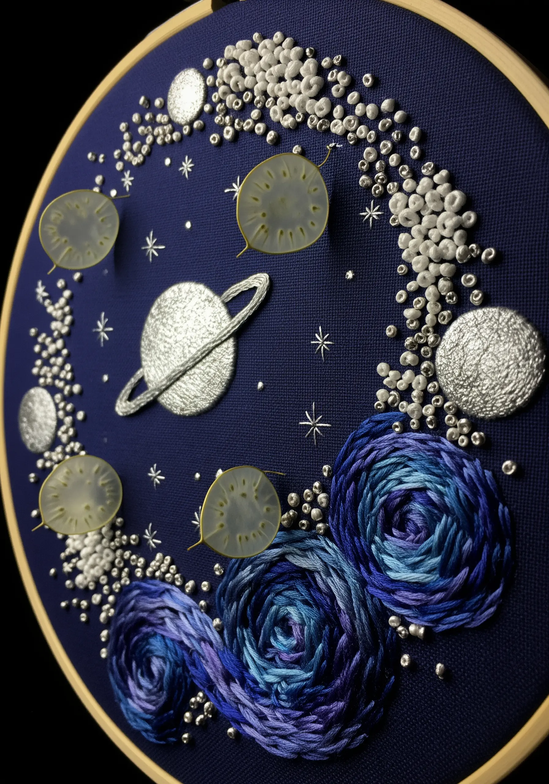 A celestial embroidery hoop with textured planets, beaded stars, and swirling thread galaxies.