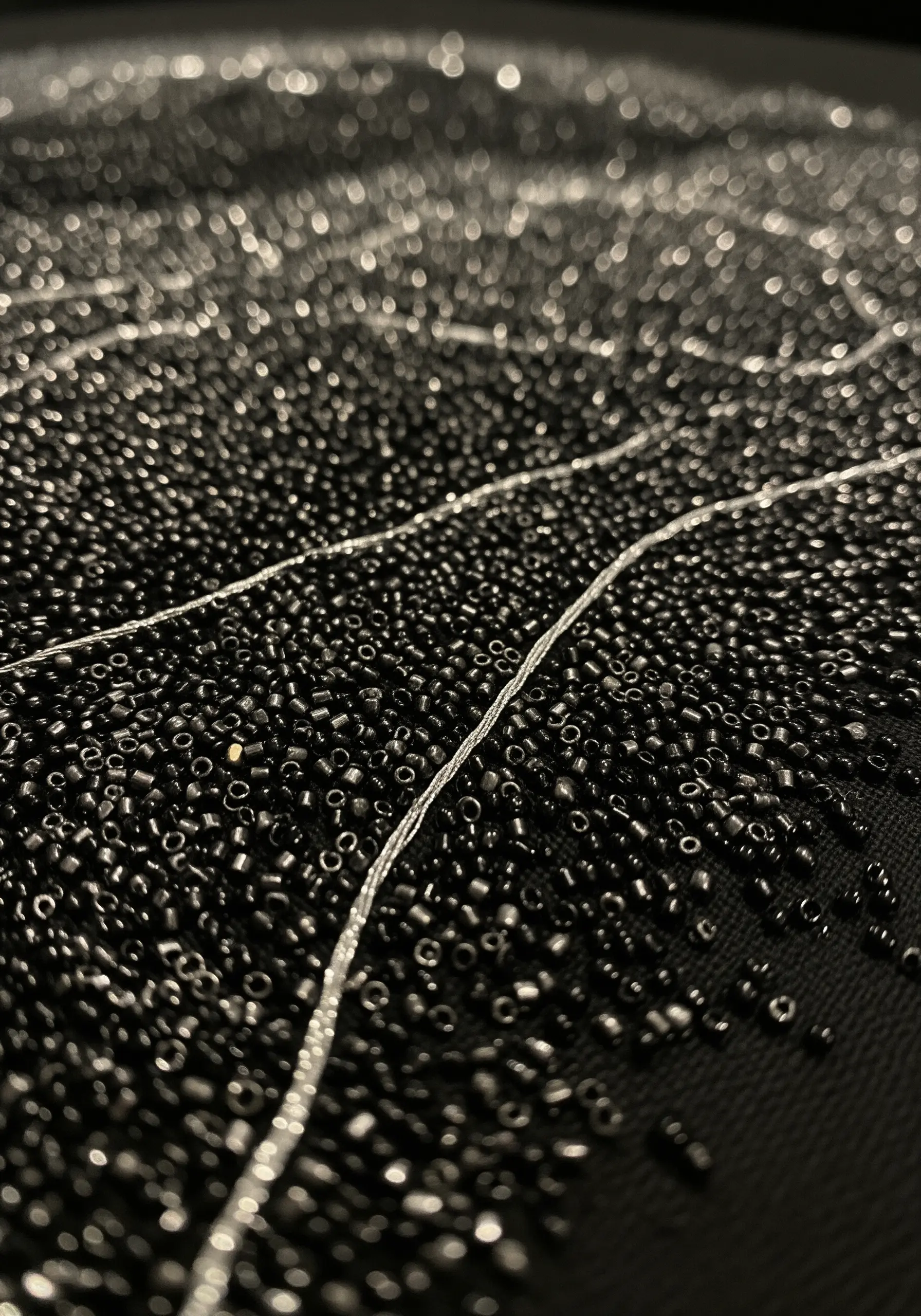 Close-up of black seed beads with fine white embroidered lines running through them.