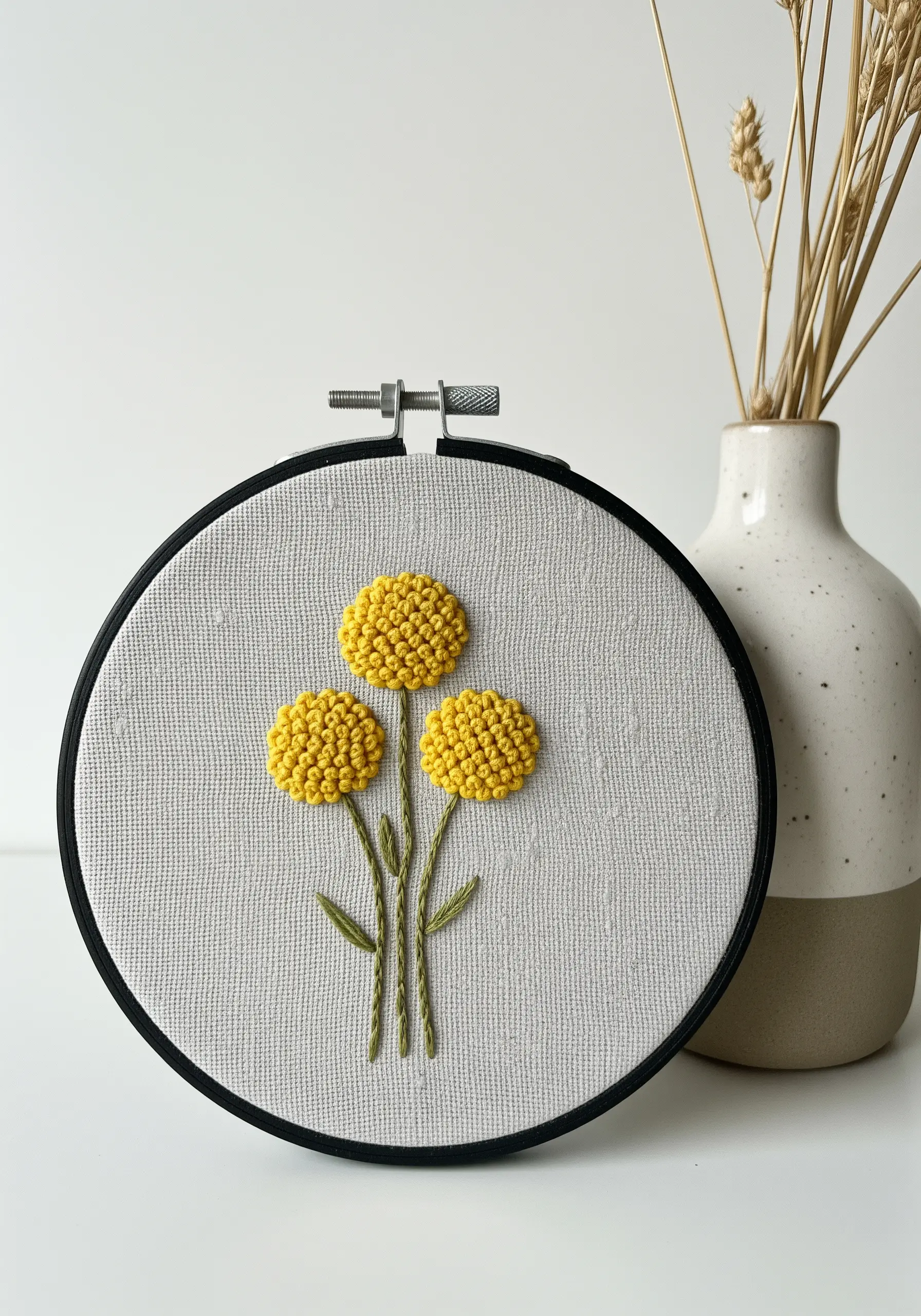 Three yellow Craspedia flowers with textured heads embroidered on light fabric