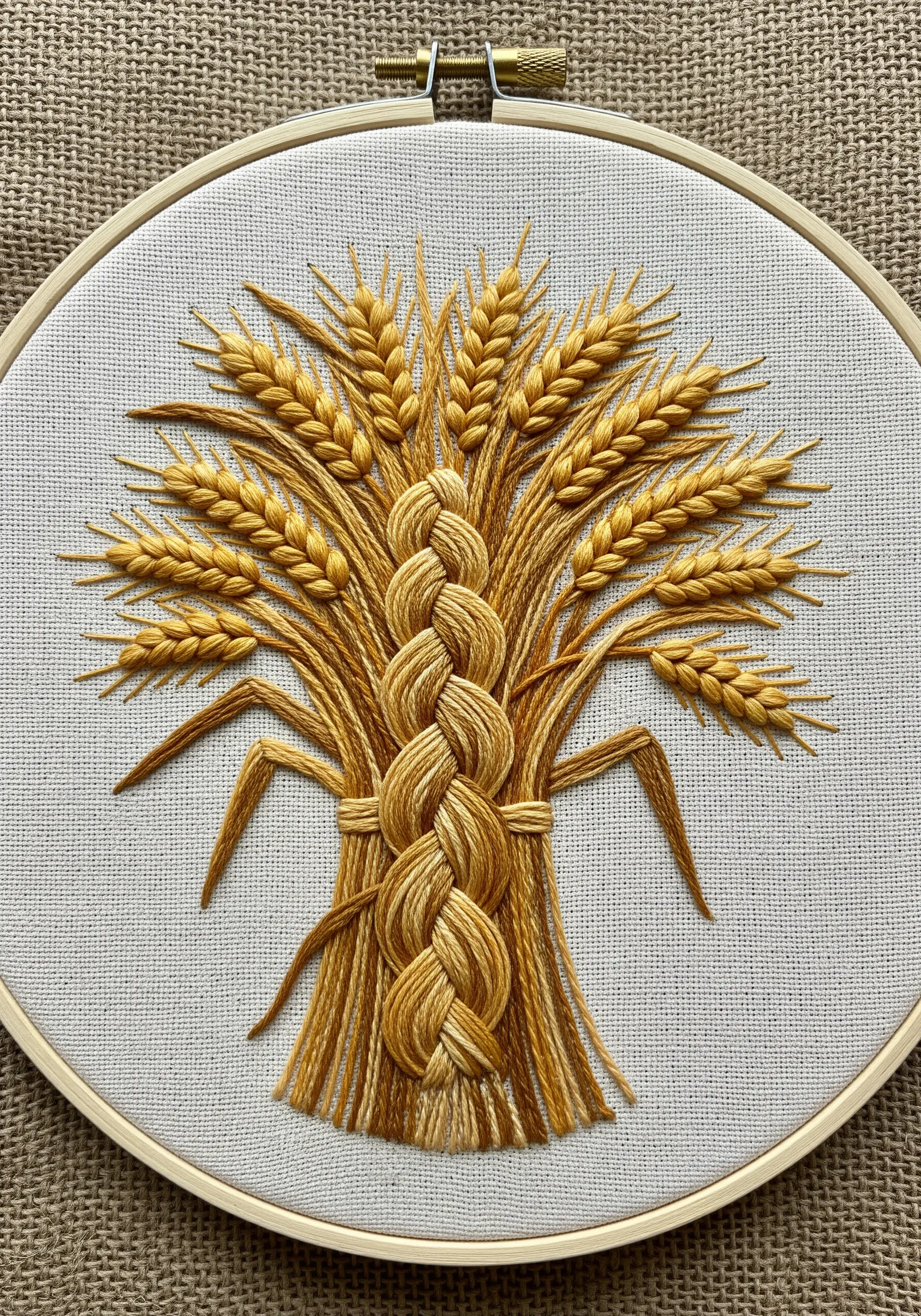 An embroidered sheaf of wheat with a central woven design using the plaited braid stitch.